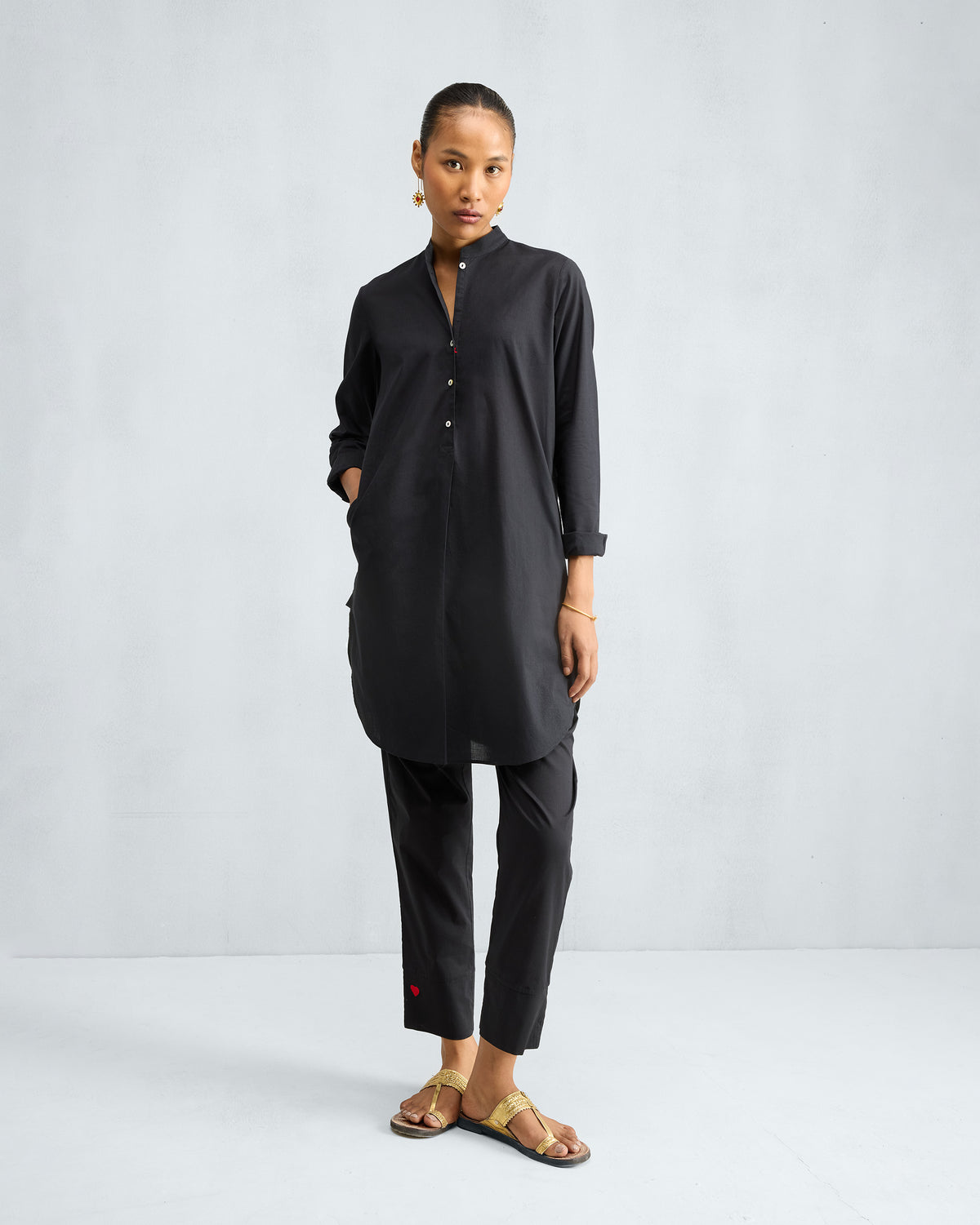 Person wearing a black mid-length kurta set with a hand in the side pocket.