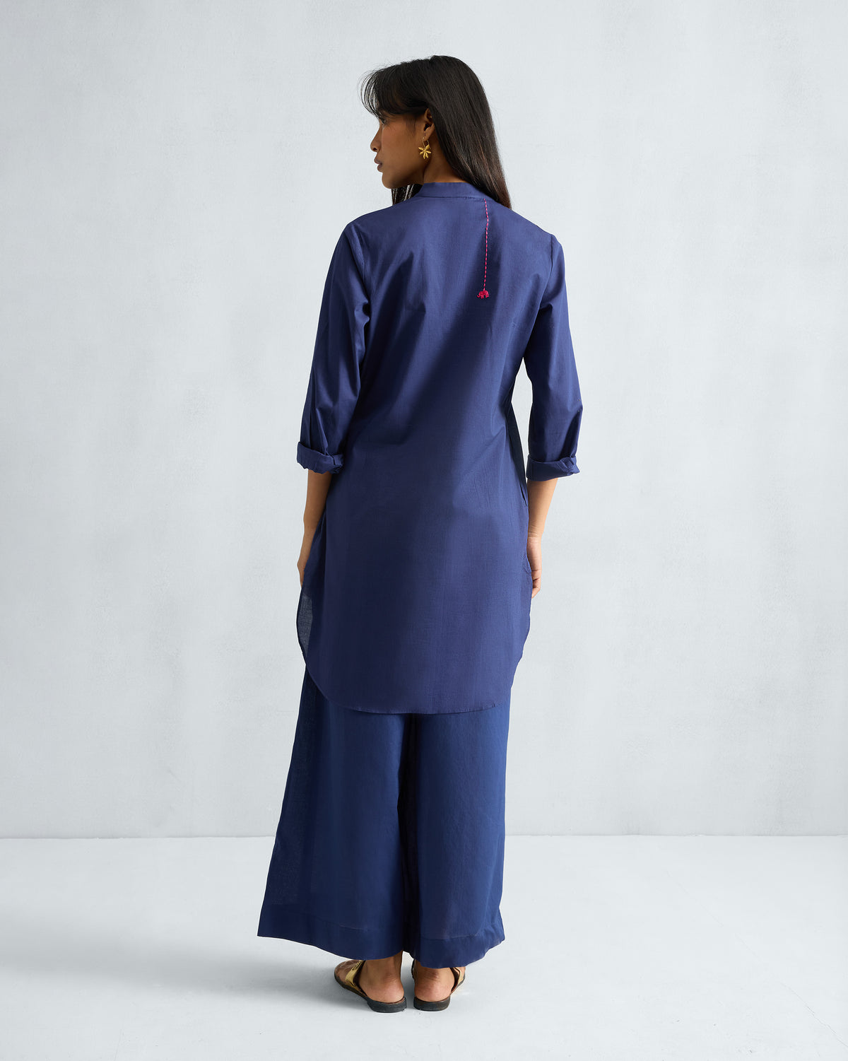 Back of an ink blue mid-length kurta set with pink embroidered detail.