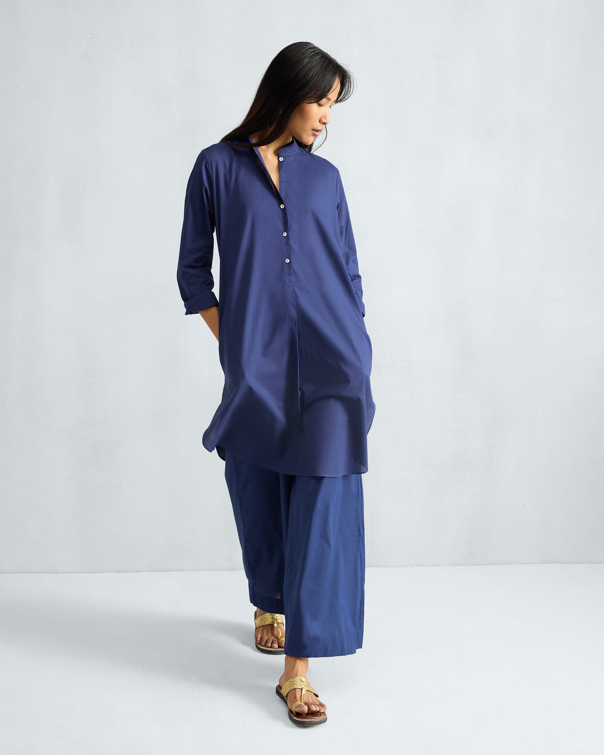 Ink blue mid-length kurta set worn with hands in the side pockets.