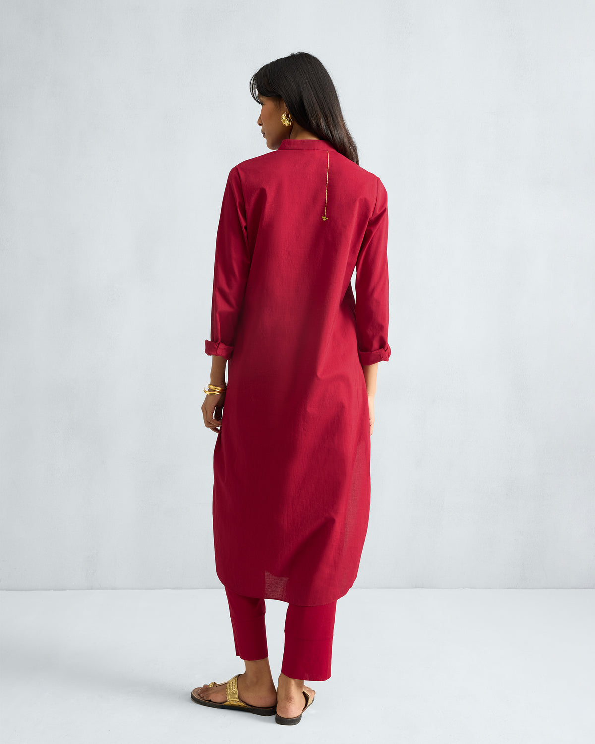 Back of a red long kurta with a vertical gold embroidery line.