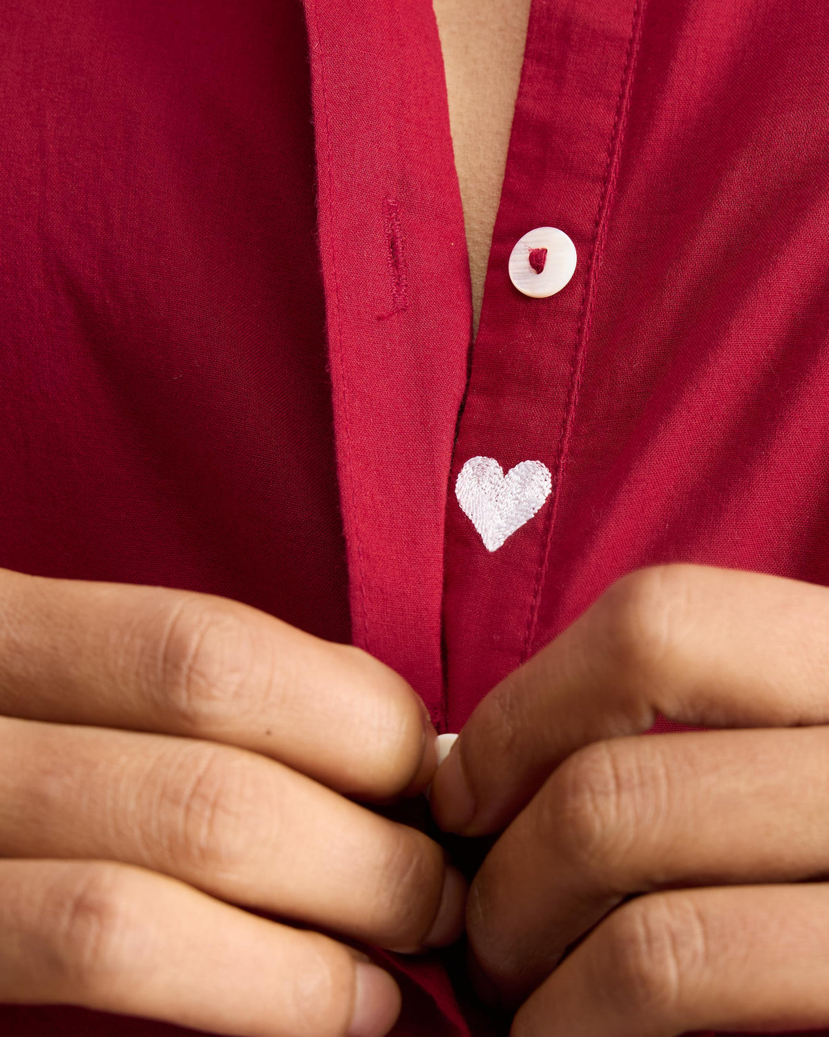 Close-up of a white heart embroidery beside a button on a red kurta.