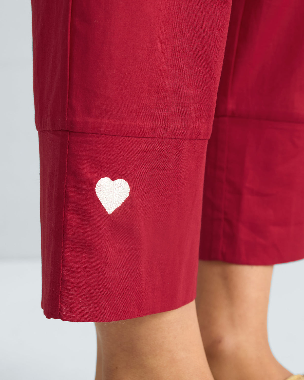 Close-up of a white heart embroidery on the hem of red trousers.