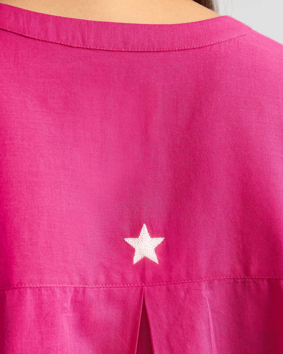 Close-up of a white embroidered star on the back of a fuchsia Lazy Sunday tunic.