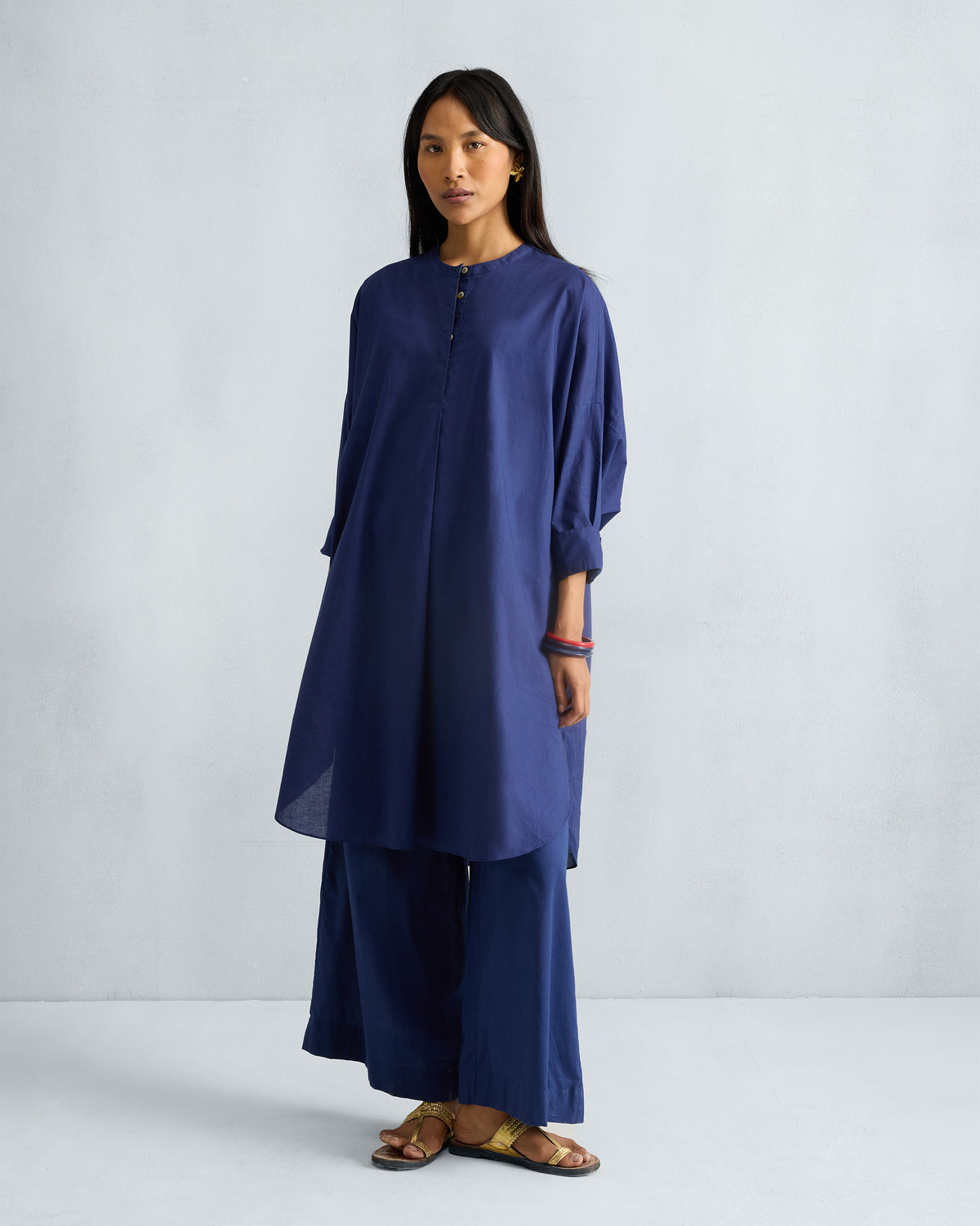 Person wearing the Lazy Sunday tunic in ink blue with a button placket at the band collar.