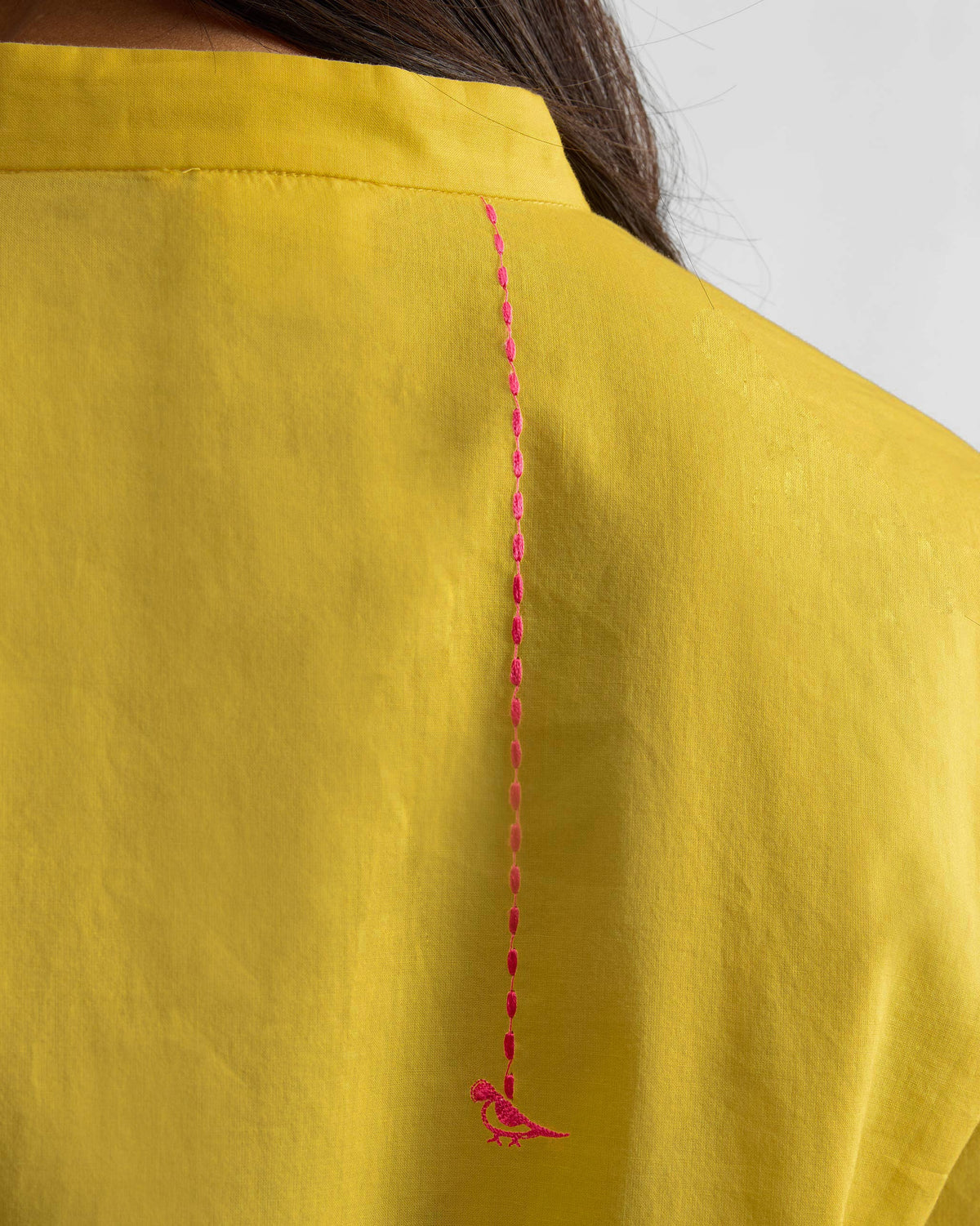 Close-up of pink bird embroidery on the back of a yellow kurta.