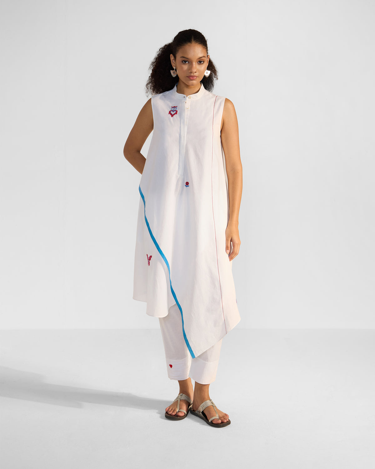 Person wearing a white Riha Kurta Set with blue selvedge trim and cross-stitch motifs.