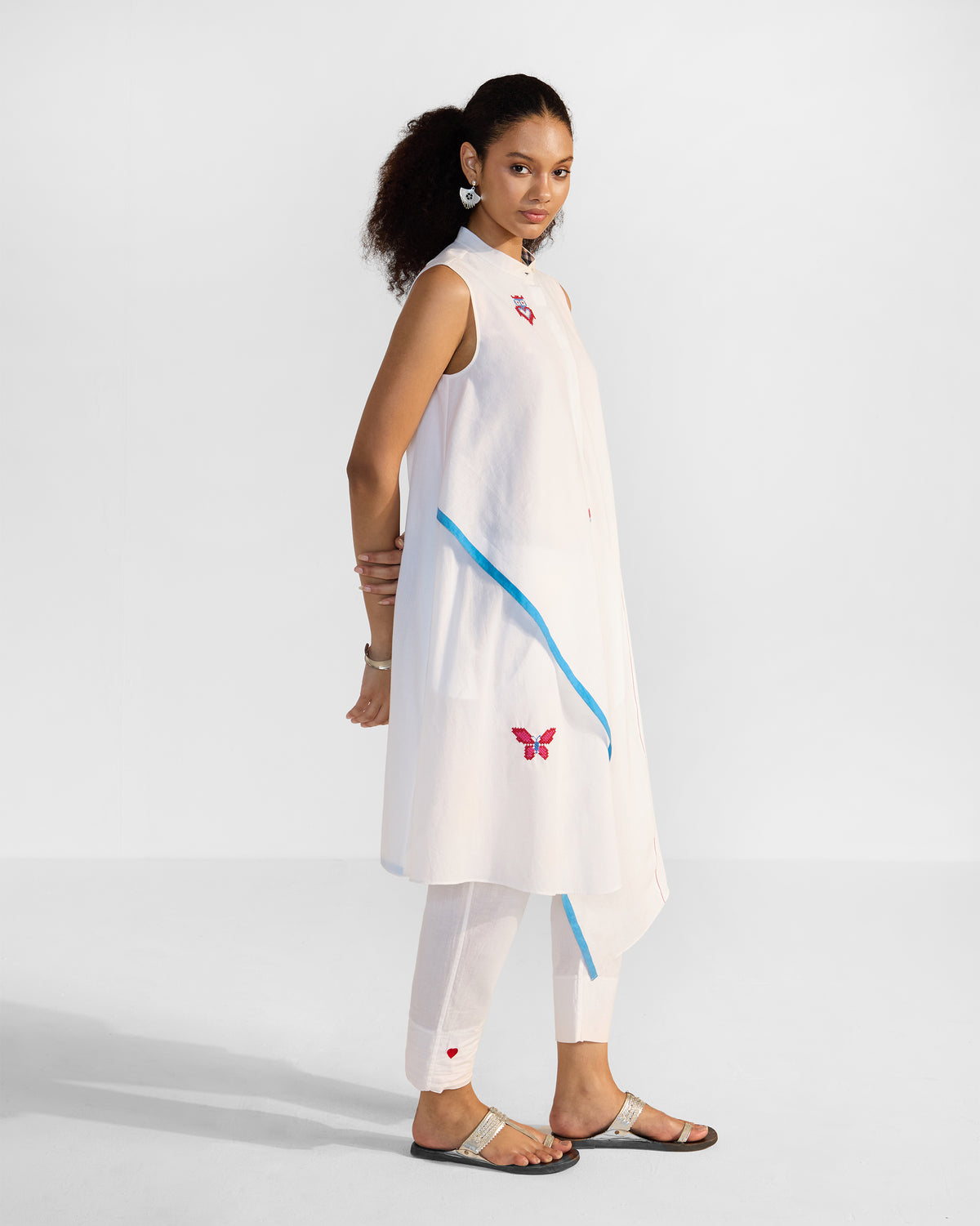 Three-quarter view of a white Riha kurta with an asymmetric hem and blue trim.