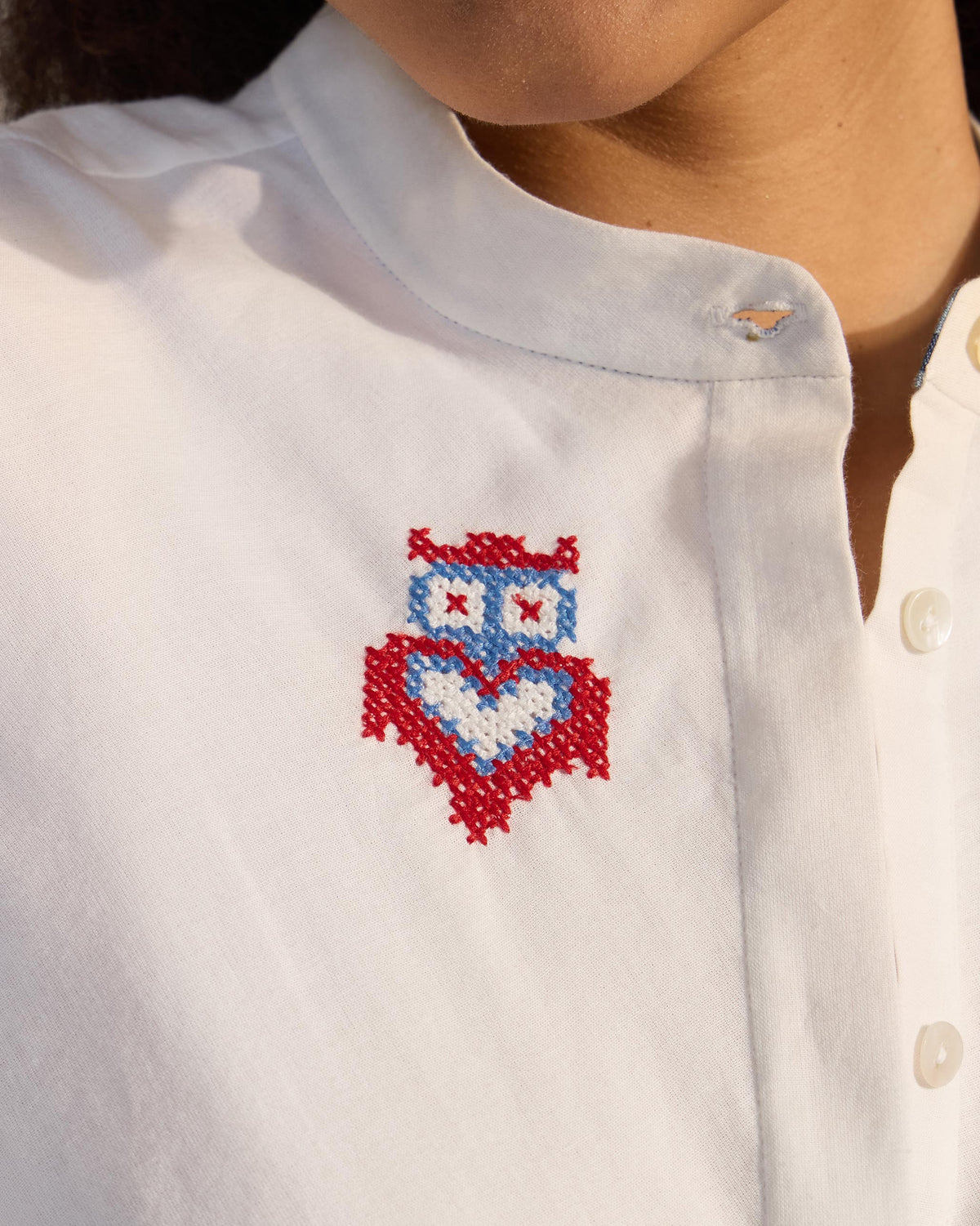 Close-up of a red and blue owl embroidery on a white Riha kurta.