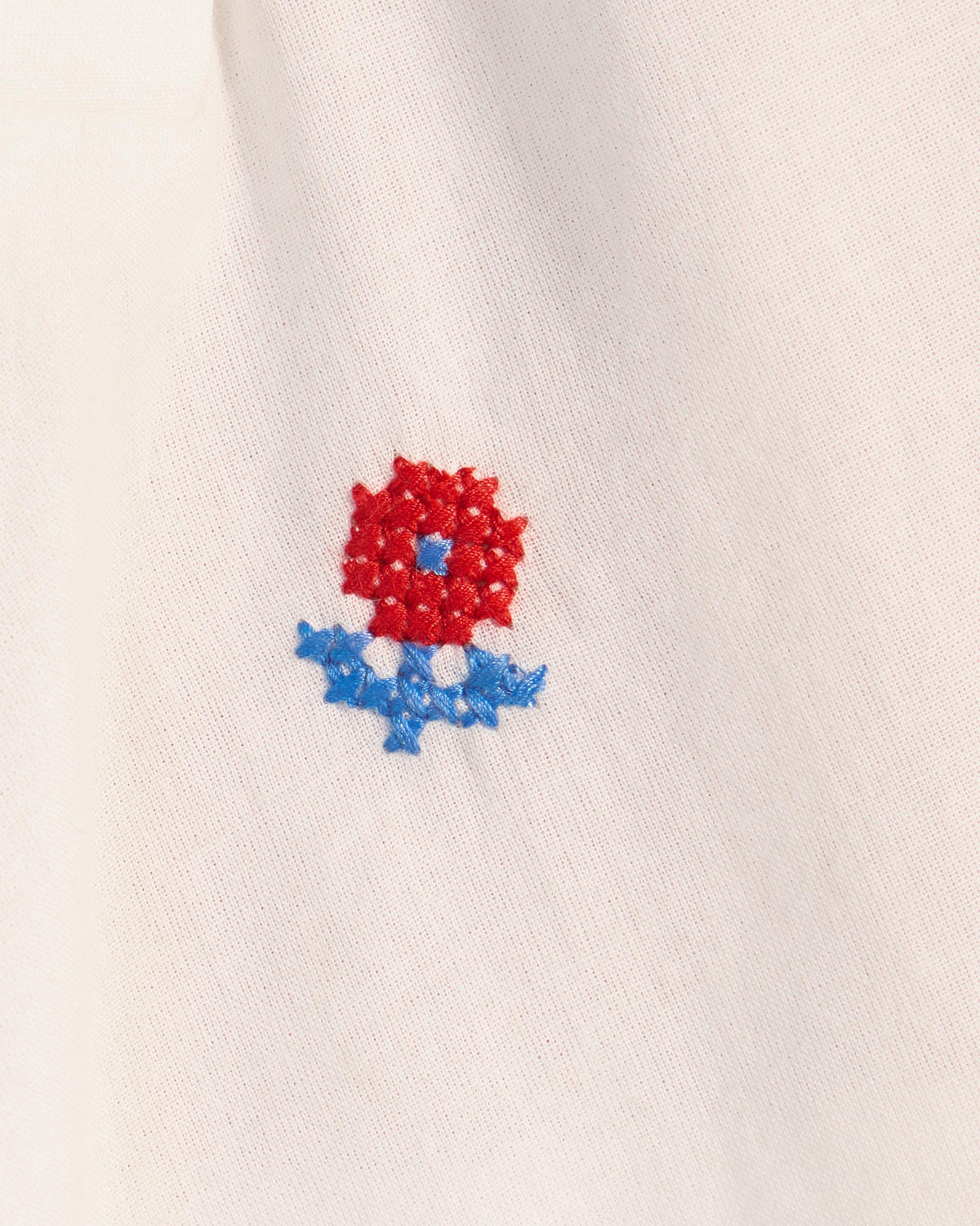 Close-up of a red flower embroidery on a white Riha kurta.