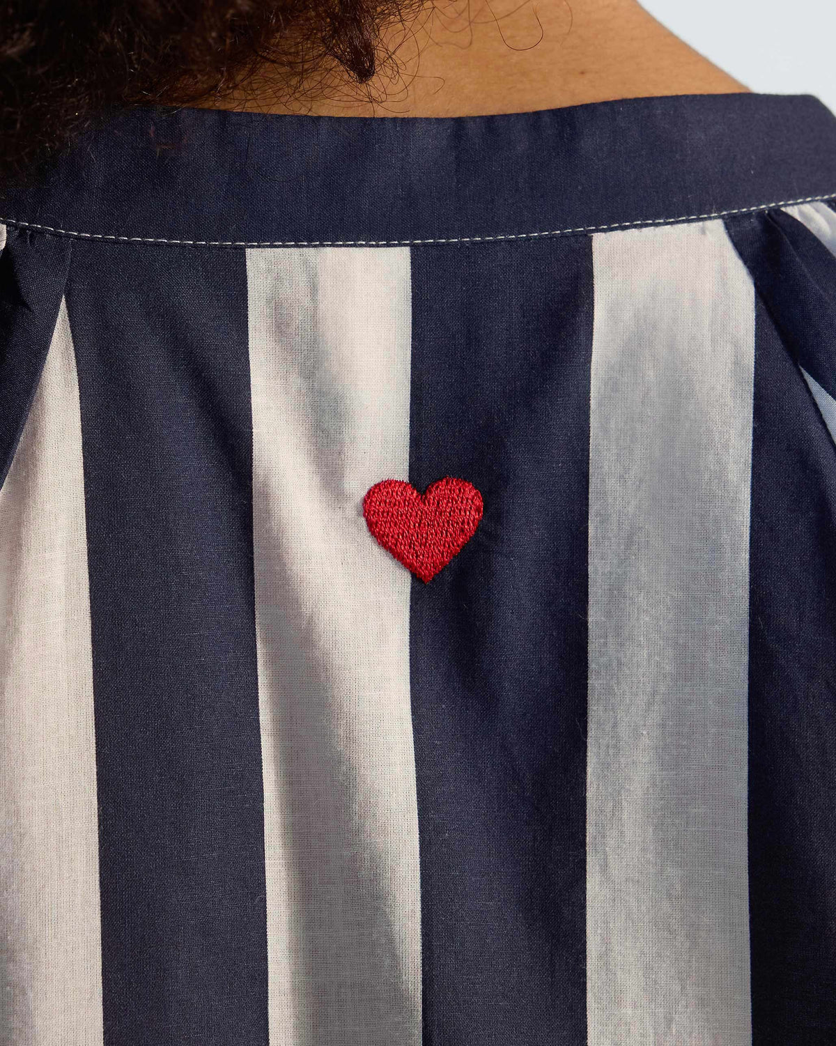 Close-up of a red heart embroidery on the back of a striped Zaya top.