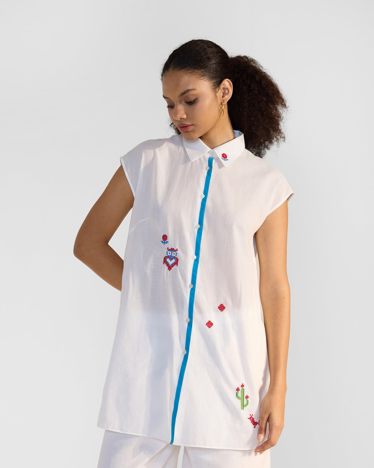 Person wearing a white Eira Top Set with blue trim and cross-stitch embroidery.