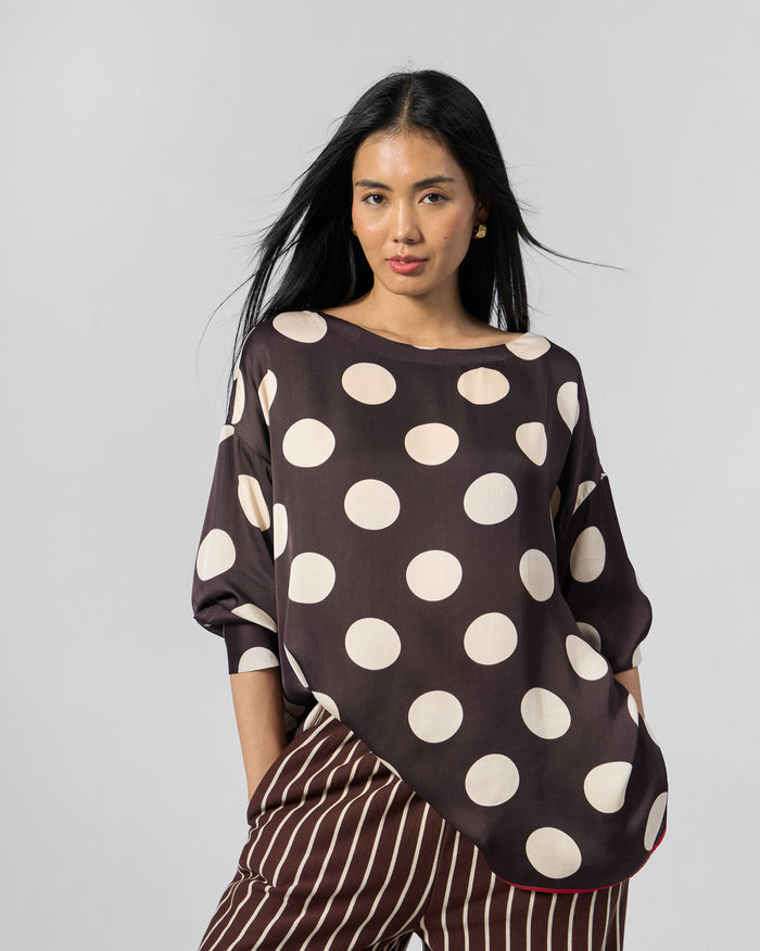 Person wearing a brown ivory polka-dot top with red hem piping.