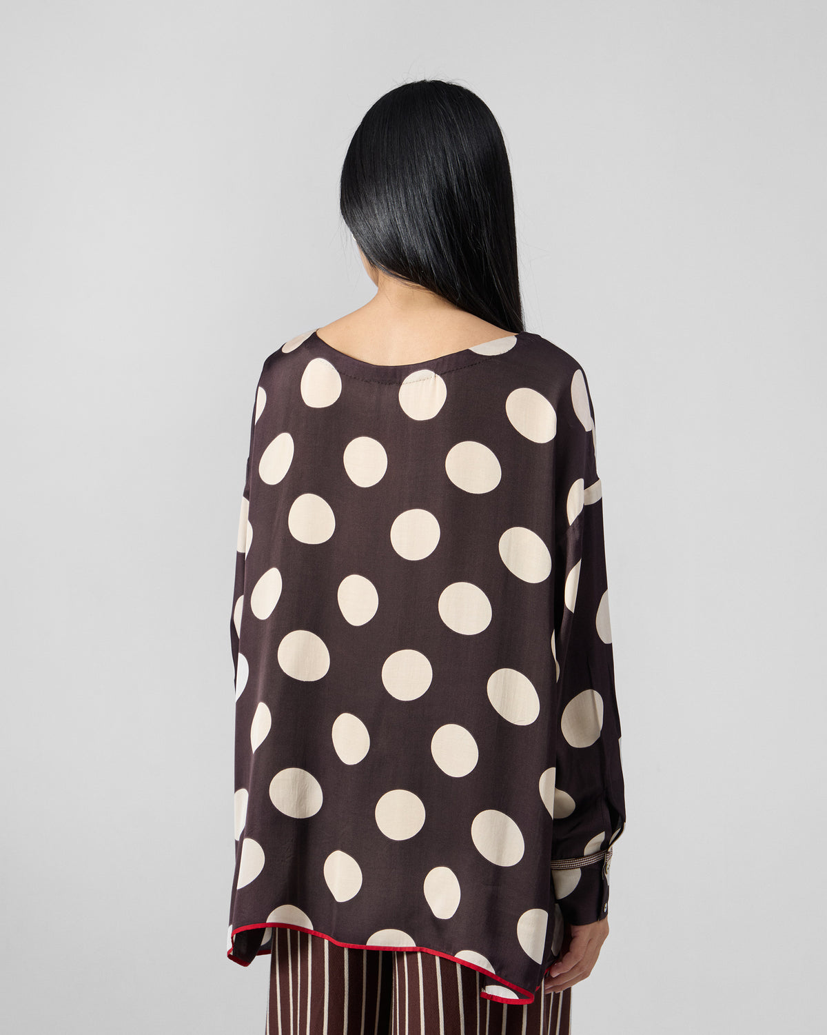 Back of a brown polka-dot top with red hem piping.