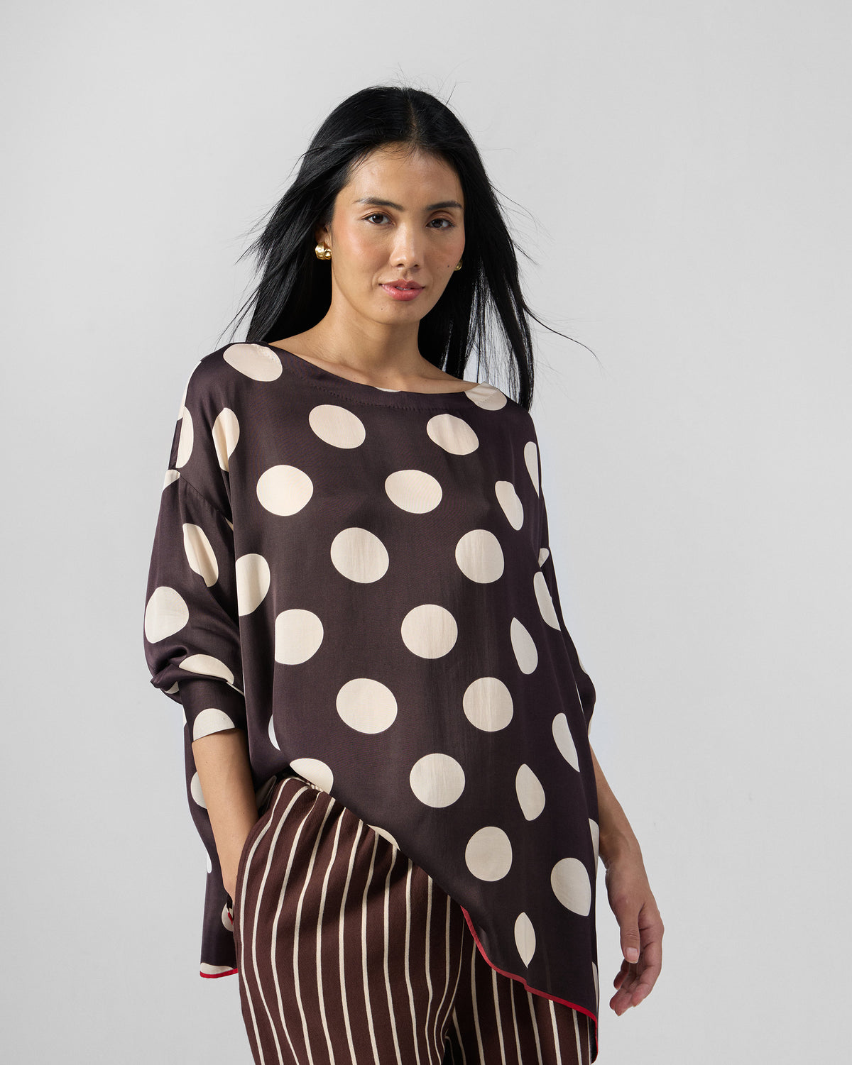Person wearing a brown ivory polka-dot top over striped pants.