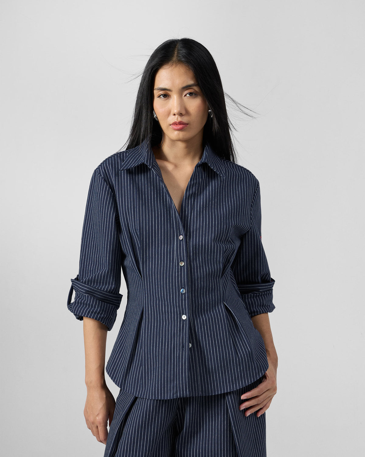 Person wearing a navy pinstripe Kalo shirt with a cinched peplum hem.