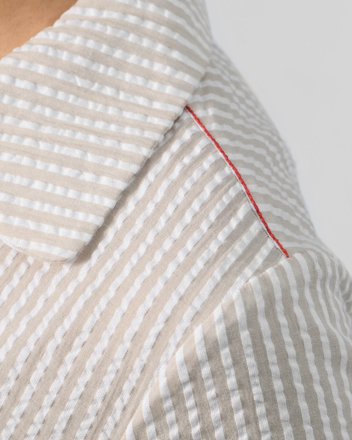 Close-up of brown and ivory seersucker fabric with a red contrast stitch.