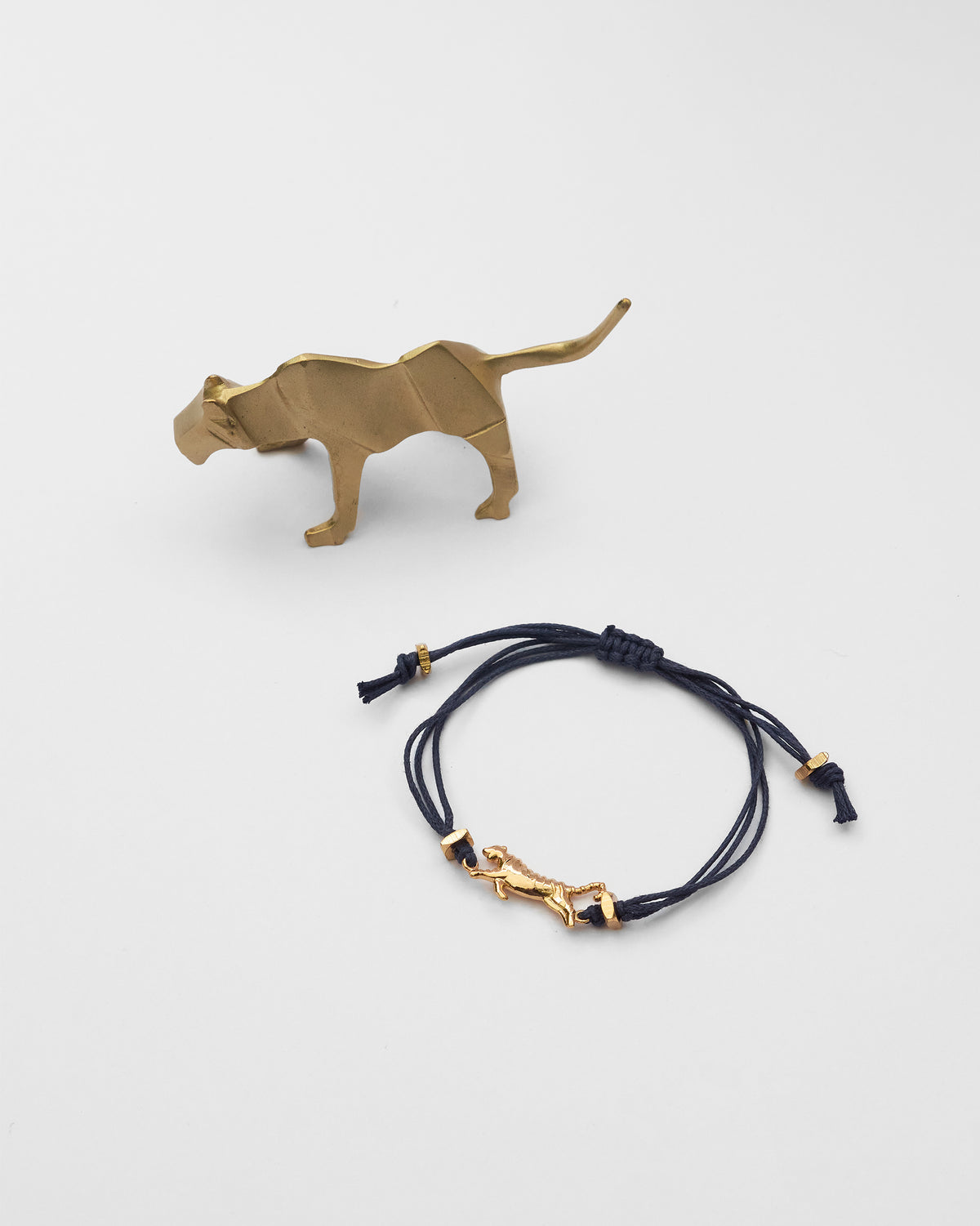 Gold tiger figurine and navy cord bracelet from the Tiger Rakhi Set, laid flat.
