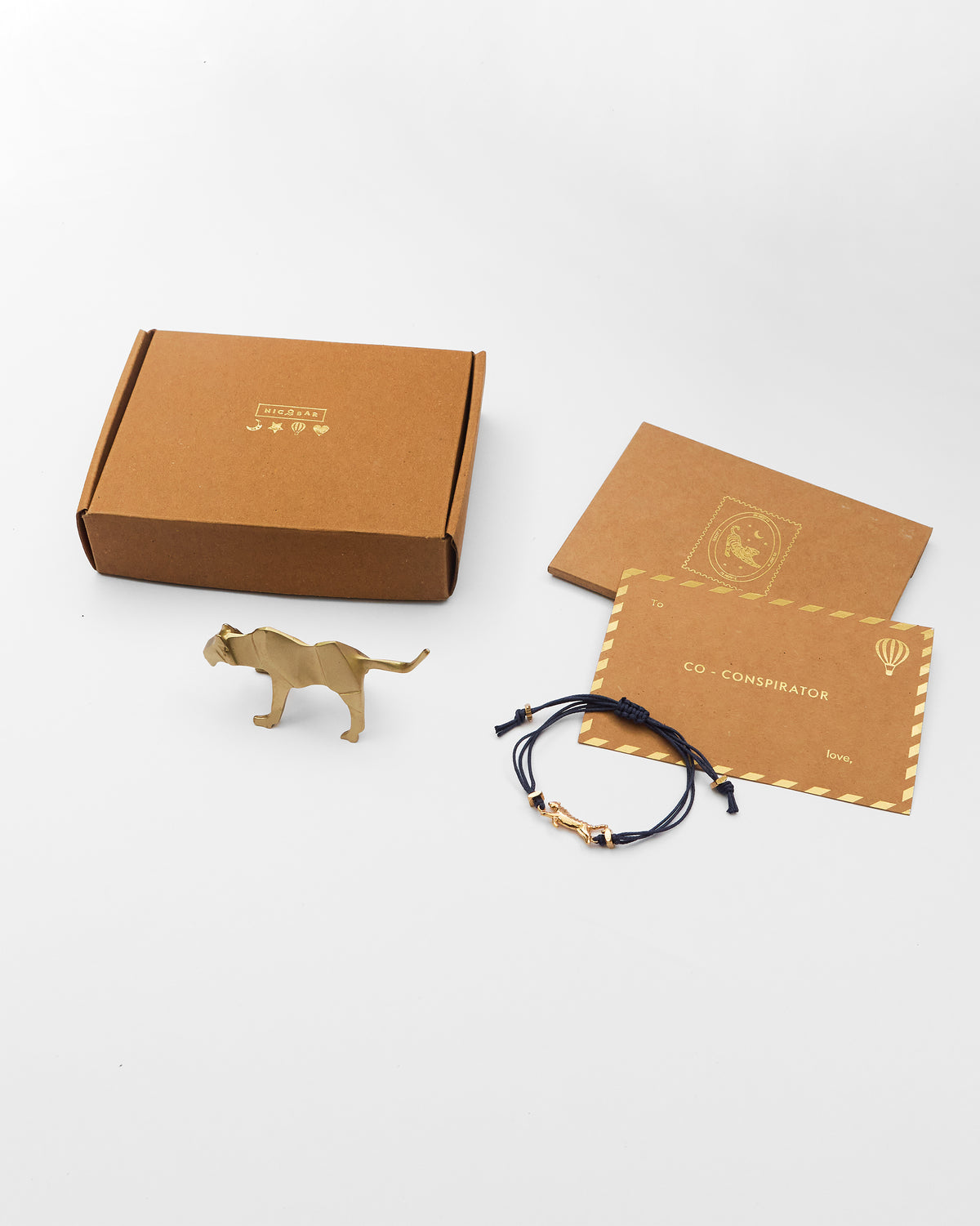Gold tiger figurine and navy bracelet from the Tiger Rakhi Set beside a kraft box and card.