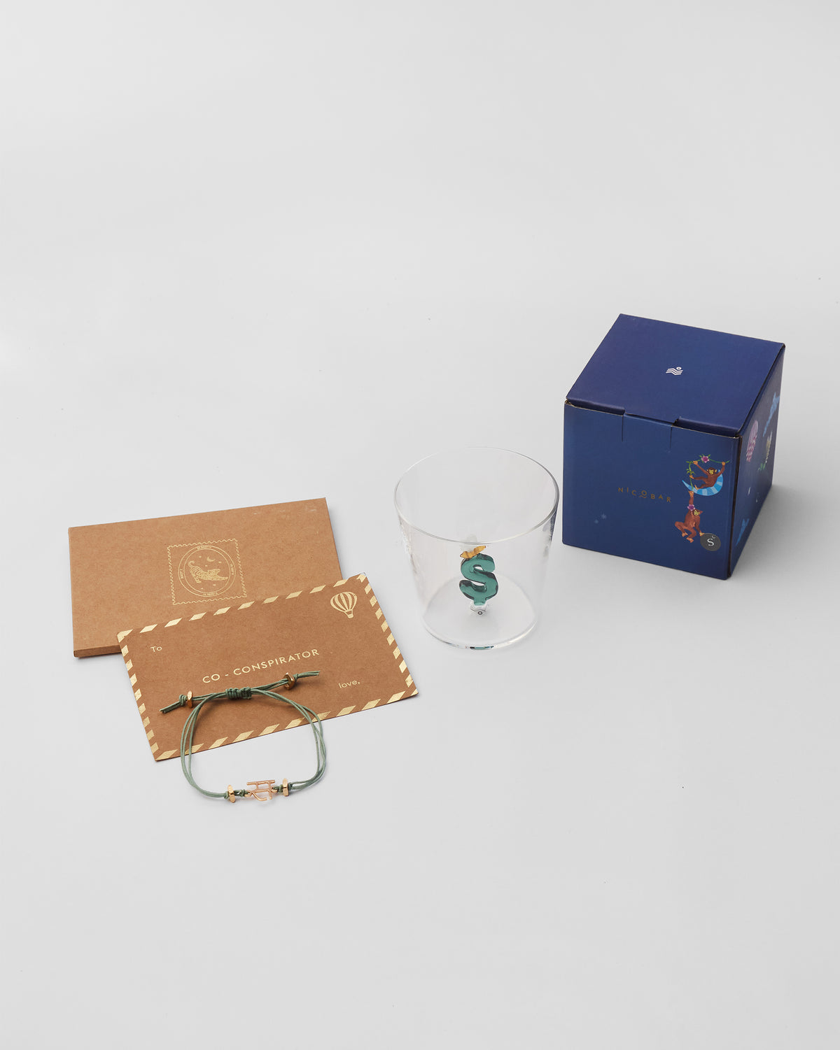Alphabet S rakhi set with glass, gift box, and envelopes.