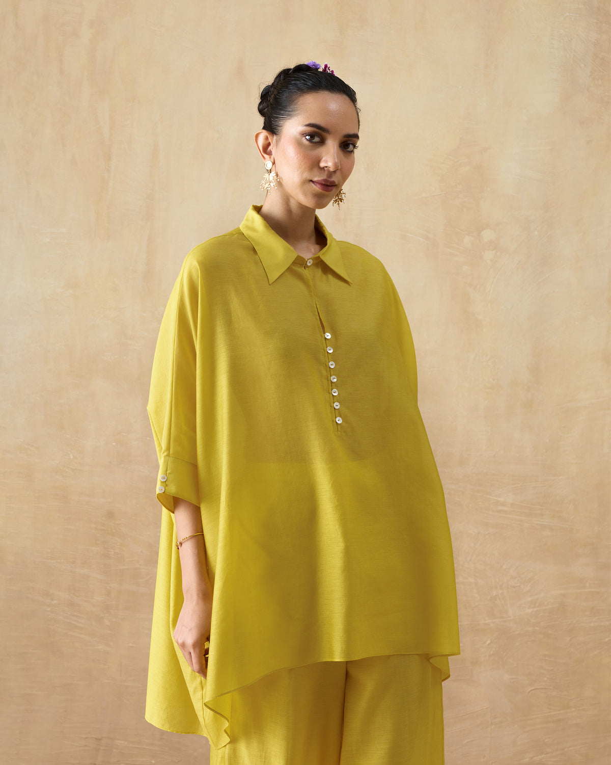 Person wearing a chartreuse oversized tunic with a pointed collar and white buttons.