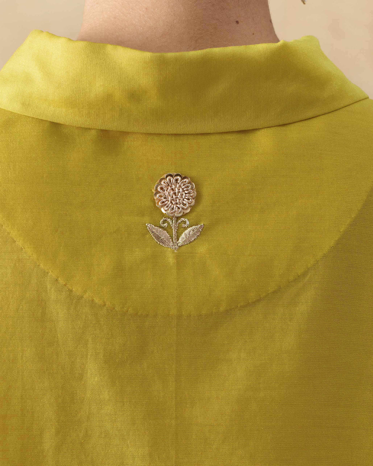 Close-up of a silver flower embroidery on the back of a chartreuse tunic.