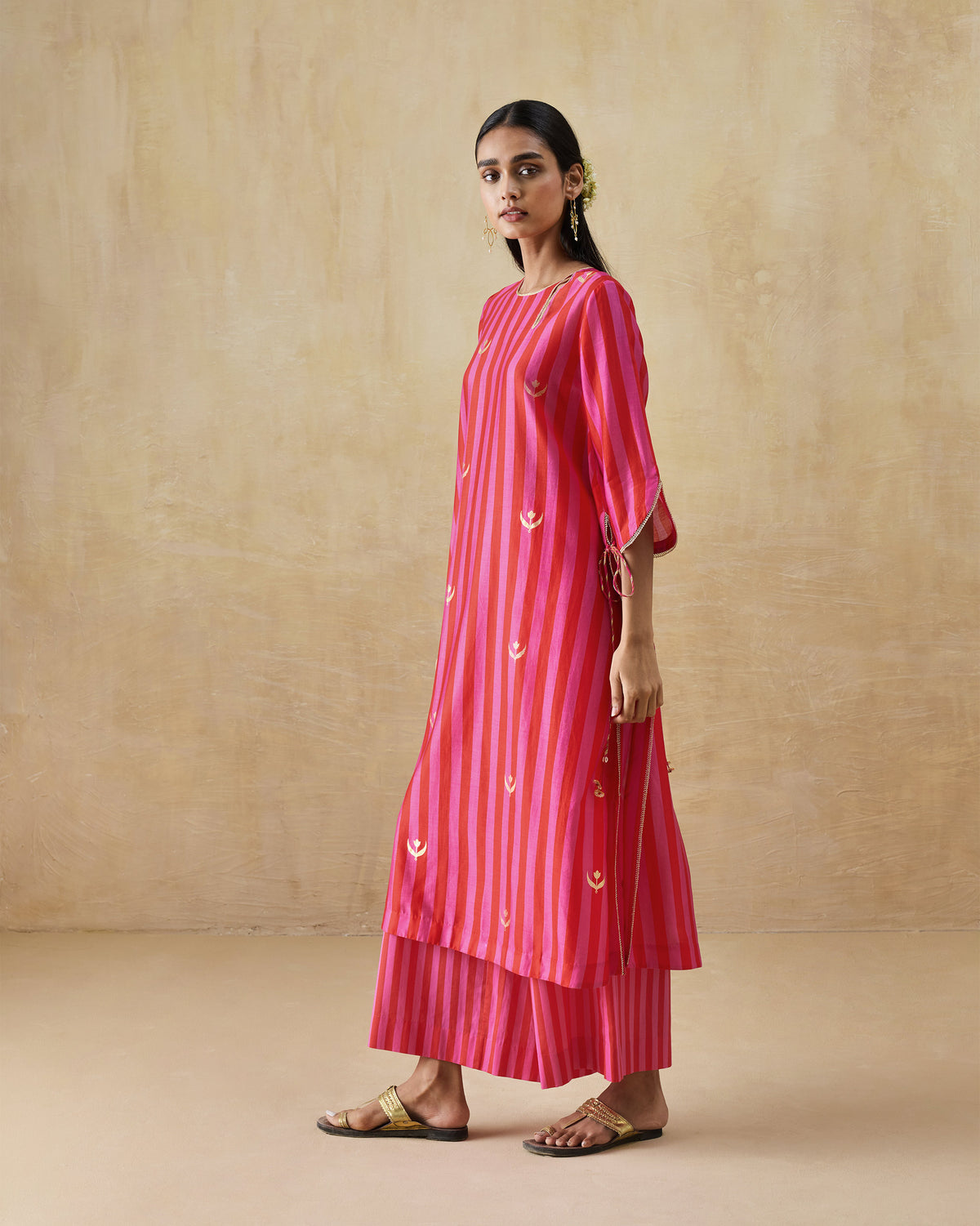 Side view of a red and berry striped kurta set with gold motifs.