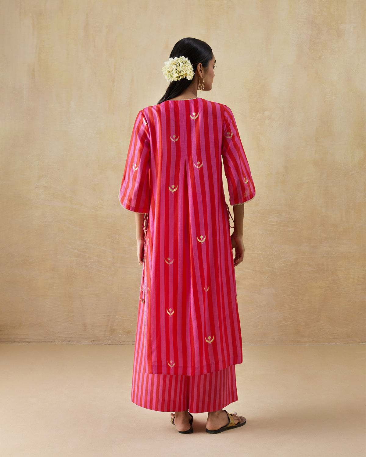 Back of a red and berry striped kurta with a center pleat and gold motifs.