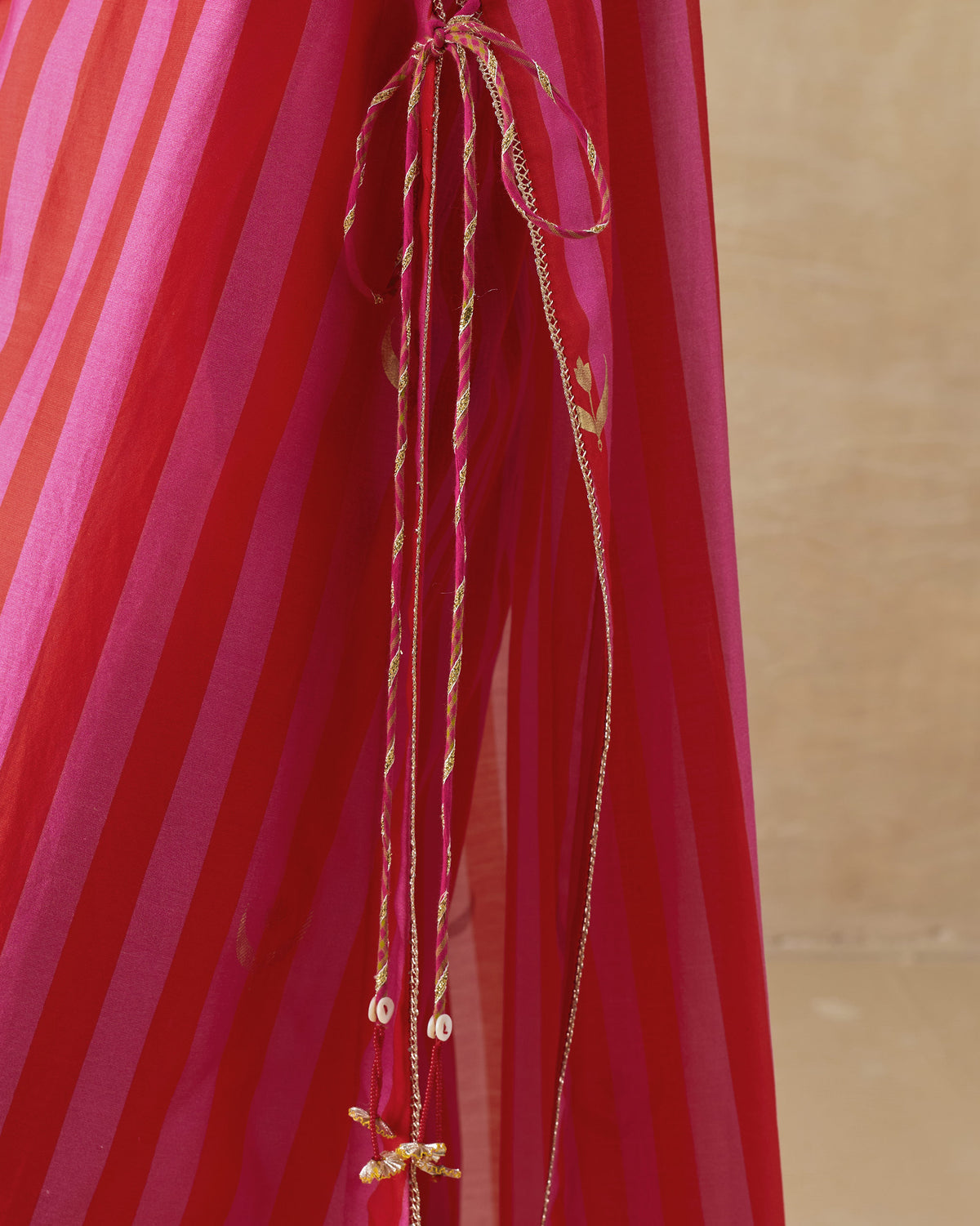 Close-up of side-tie tassels on a red and berry striped kurta.