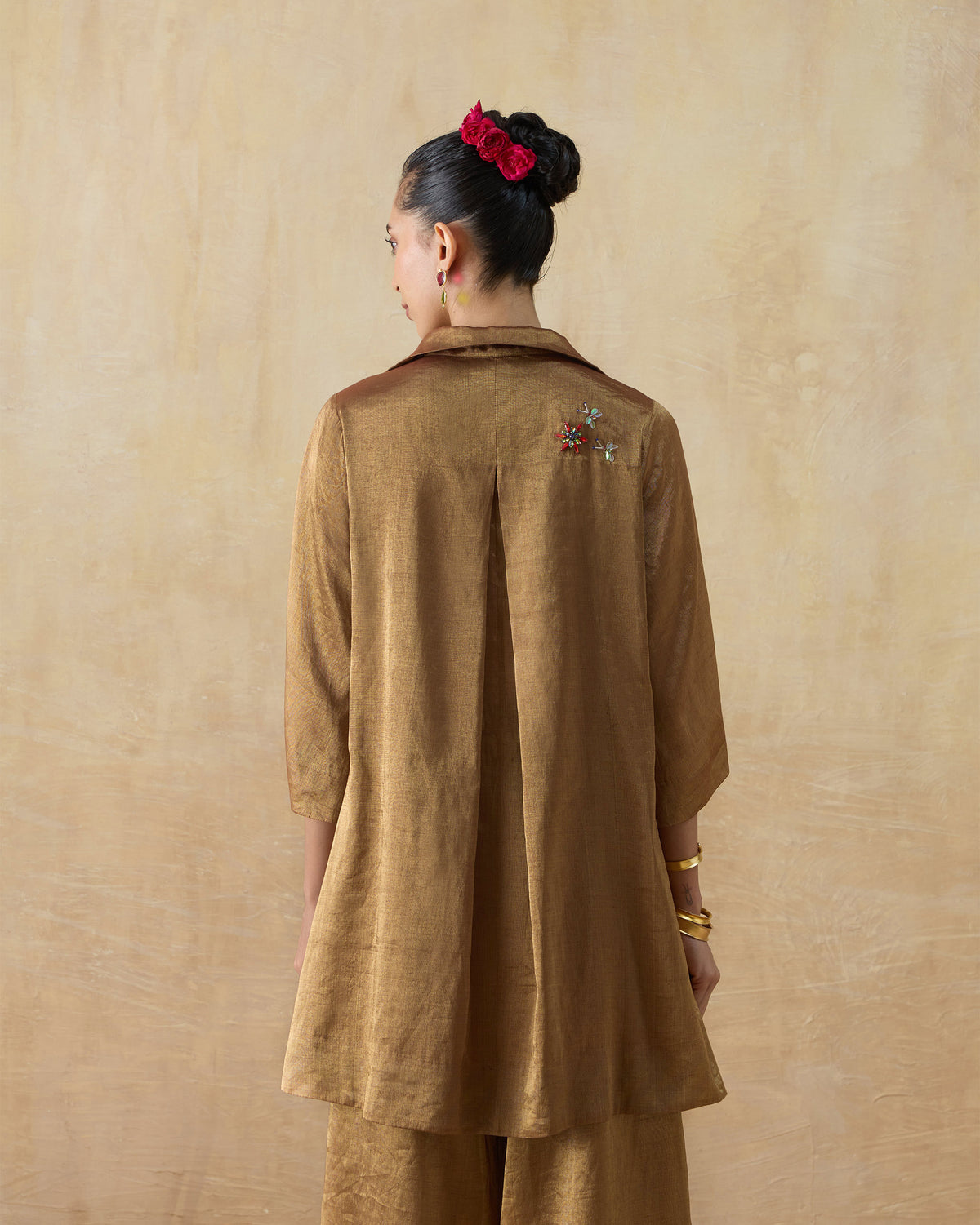 Back of a metallic gold shirt with a box pleat and floral embroidery.