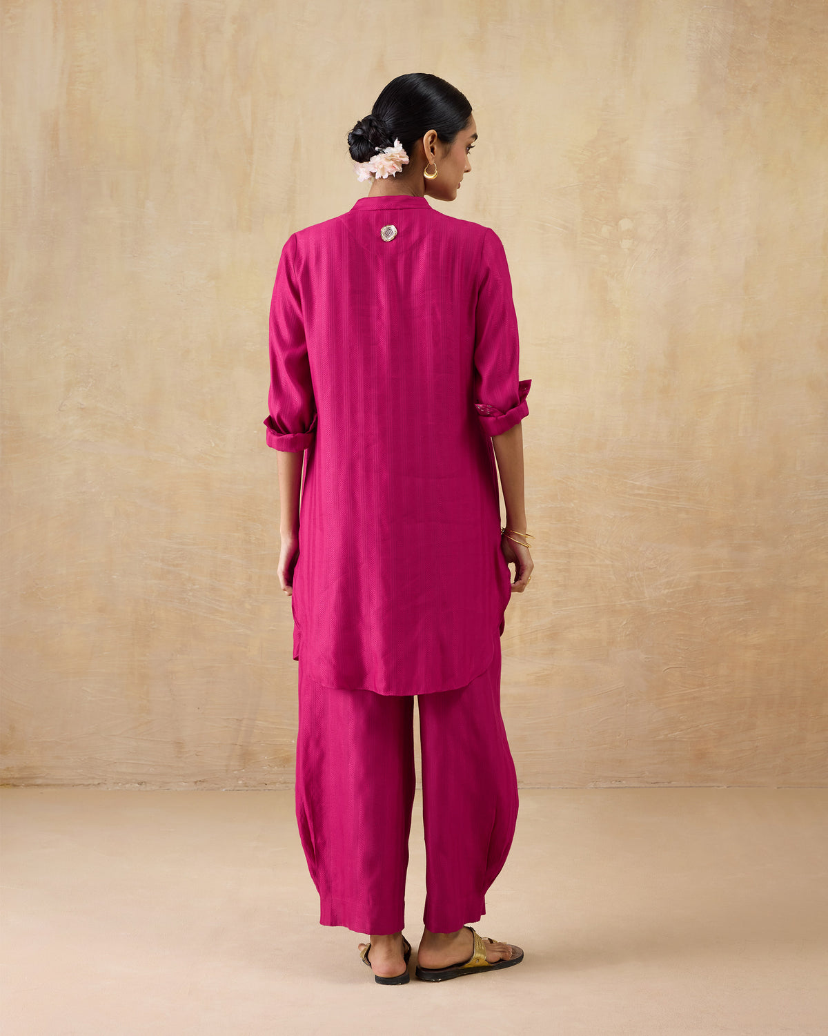 Back of a berry pink long kurta set with a curved hem and matching pants.
