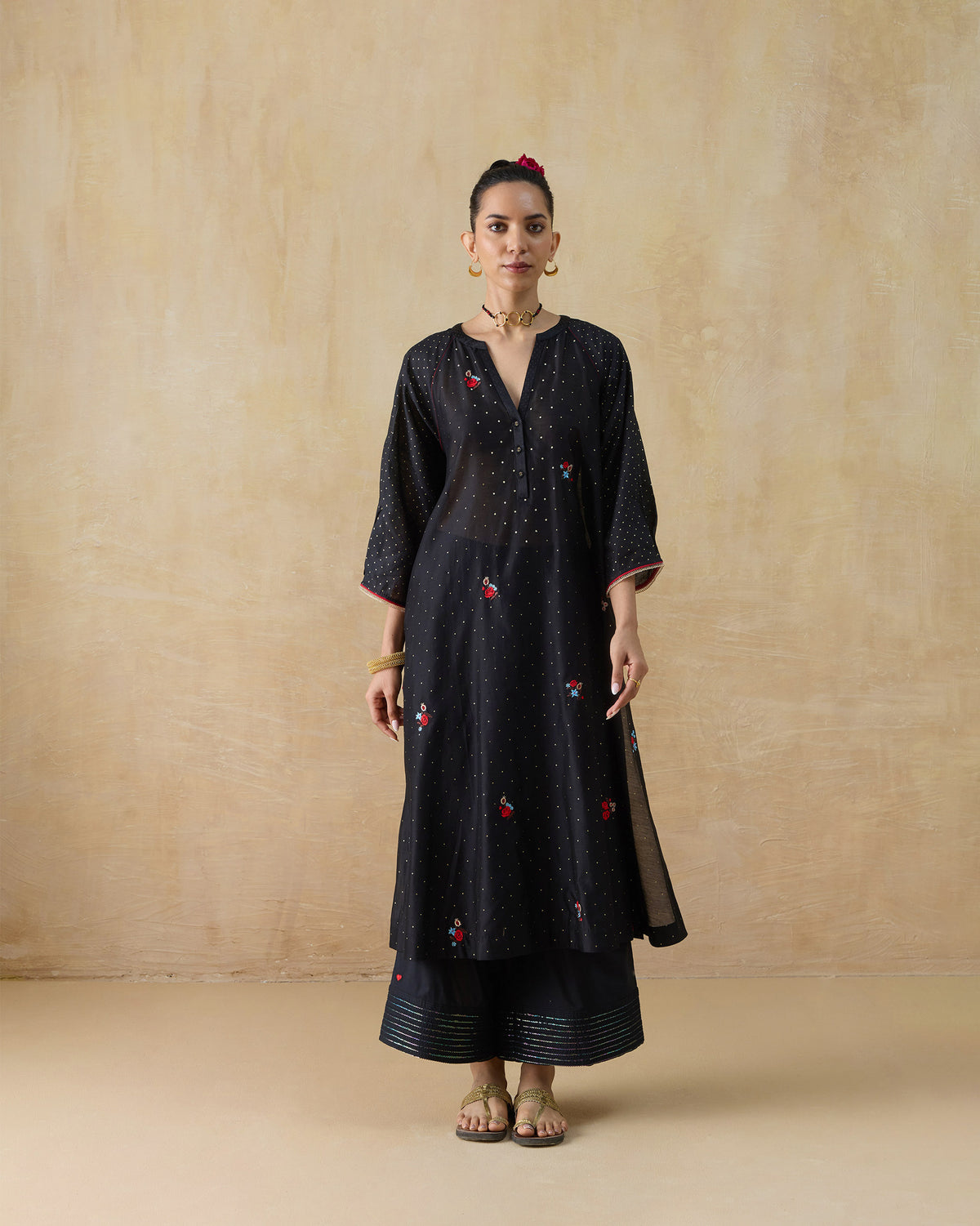 Person wearing a black Moonbeam kurta set with gold dots and red floral embroidery.
