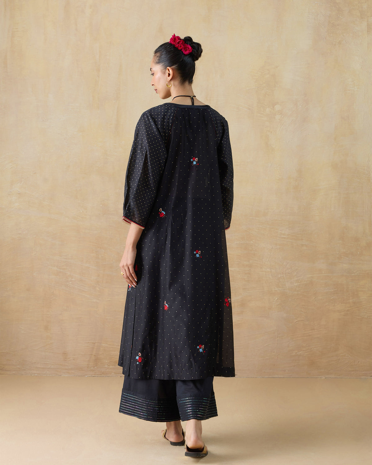 Back of a black Moonbeam kurta with scattered floral embroidery and striped pant hems.