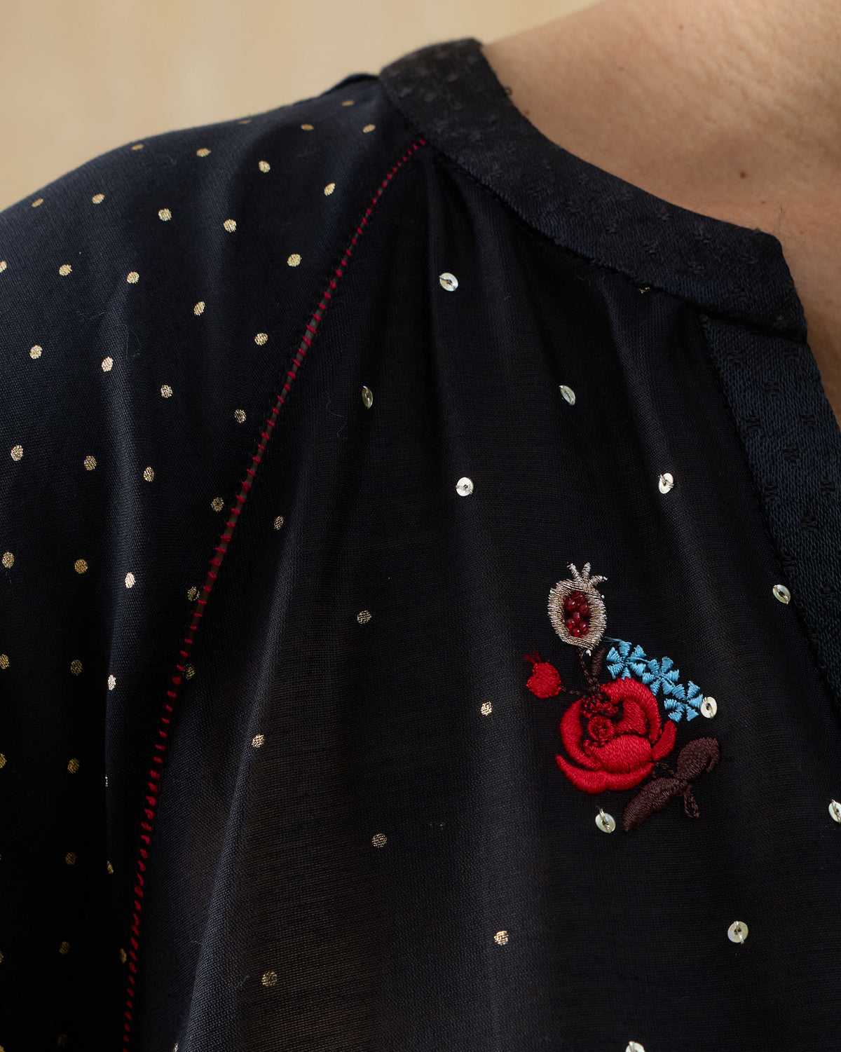 Close-up of Moonbeam kurta embroidery with a red rose motif and gold dots.