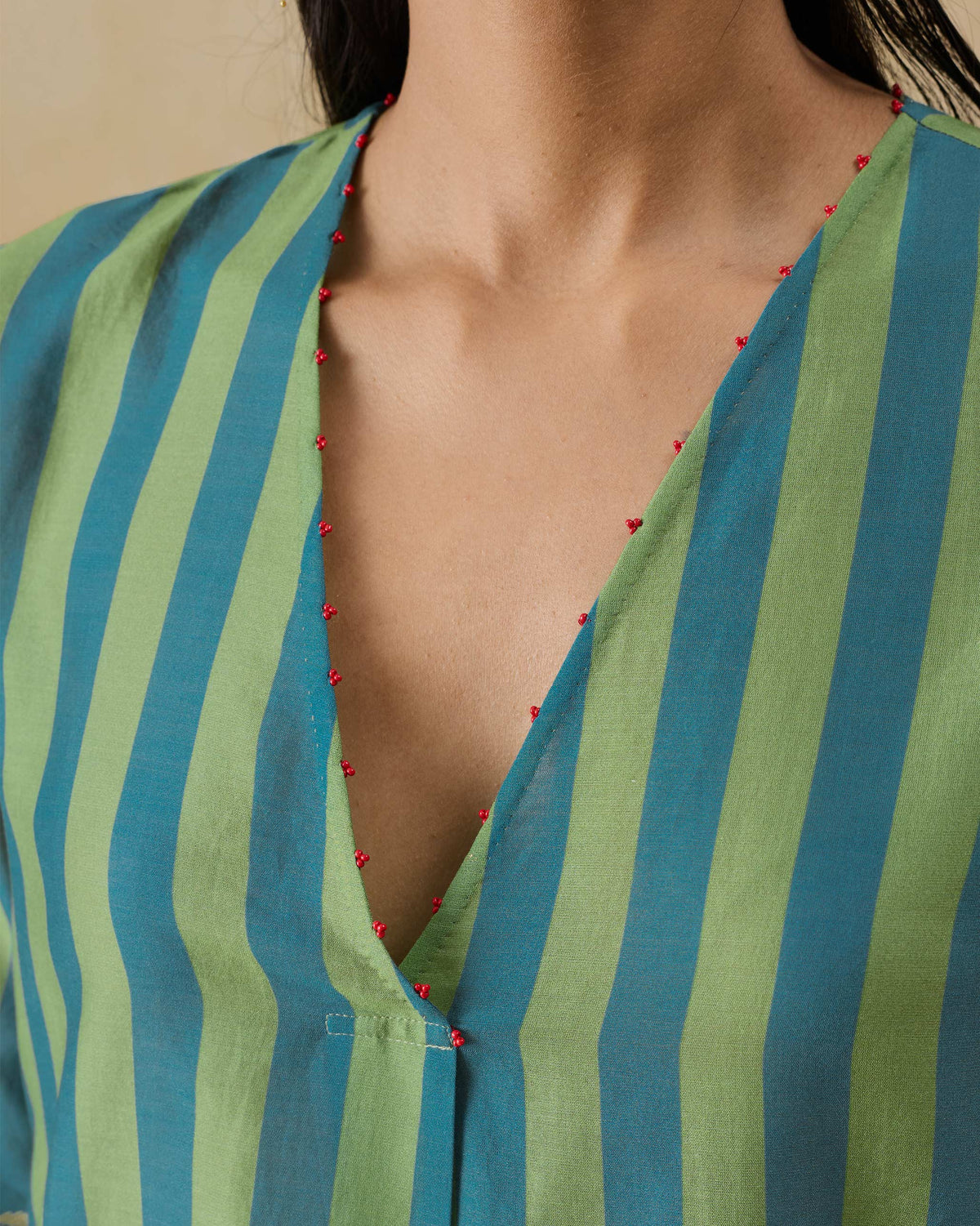Close-up of a red-beaded V-neck on a green and teal striped kurta.