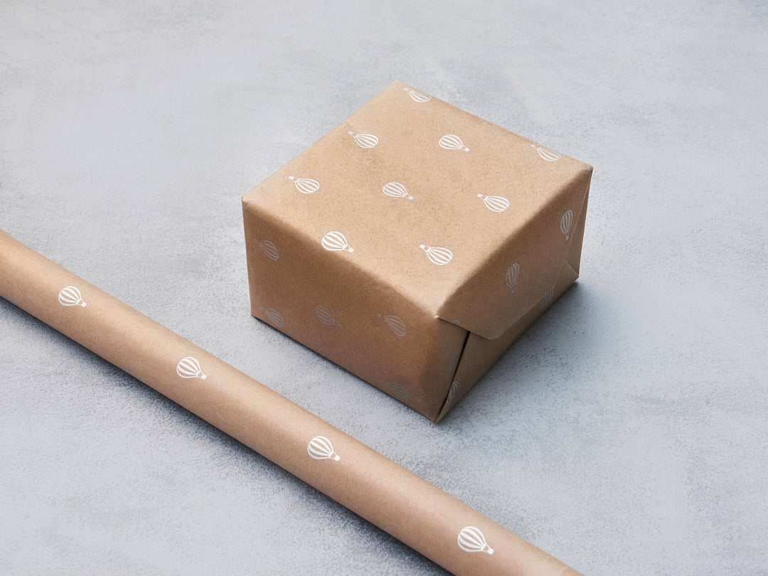 Kraft gift wrap with white hot air balloon motifs, shown on a box and a roll.