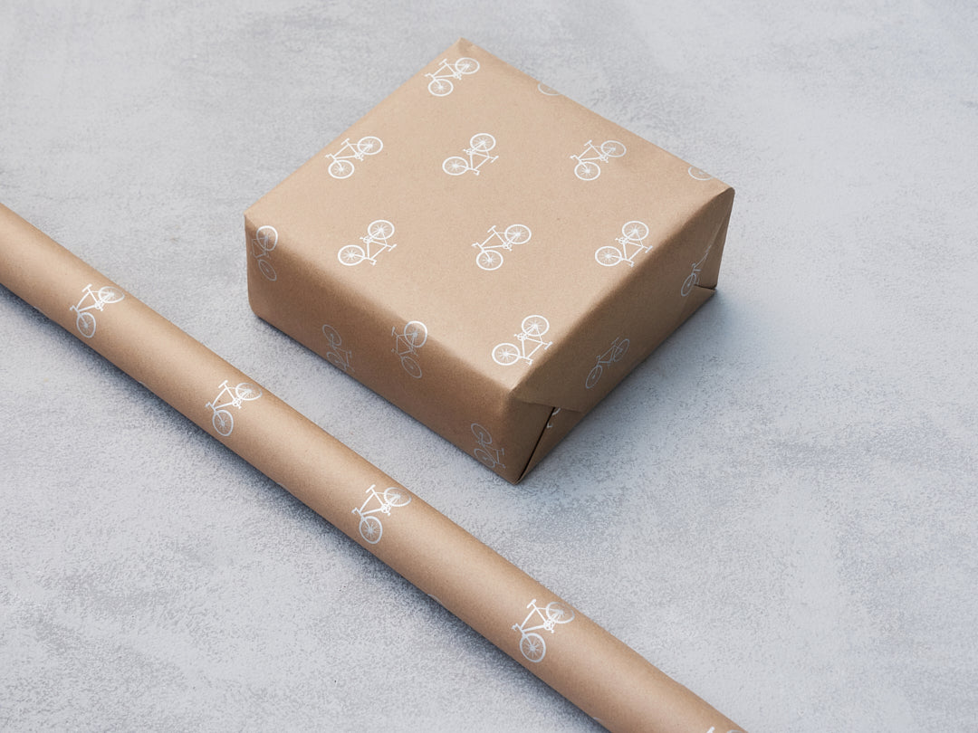 Kraft gift wrap with white bicycle motifs, shown on a box and a roll.