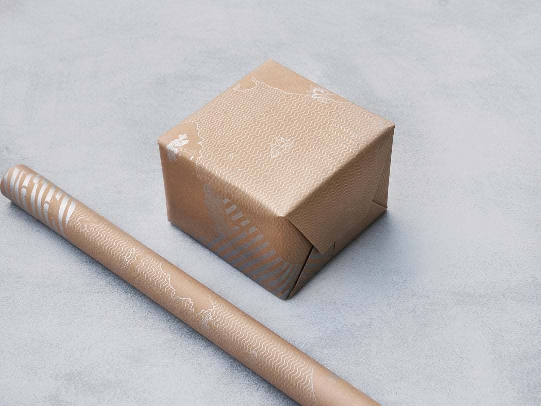 Kraft gift wrap with a pale print, shown on a box and a roll.