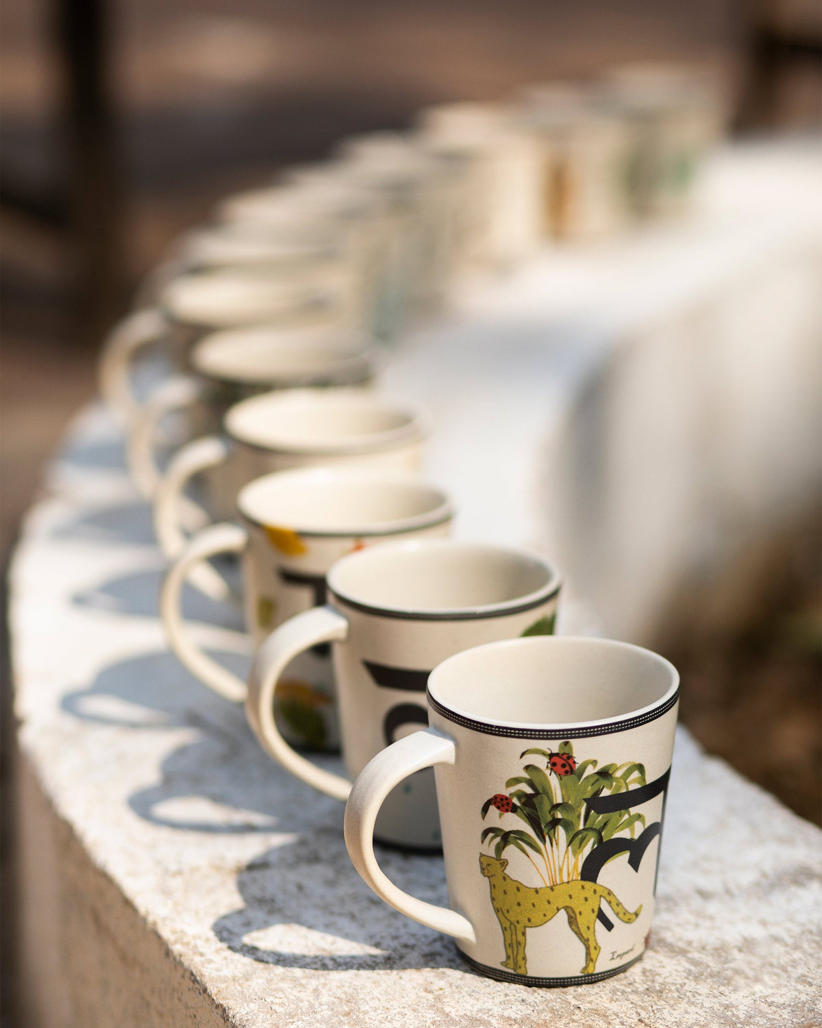 Row of Nicobar alphabet ceramic mugs lined up on a stone ledge.