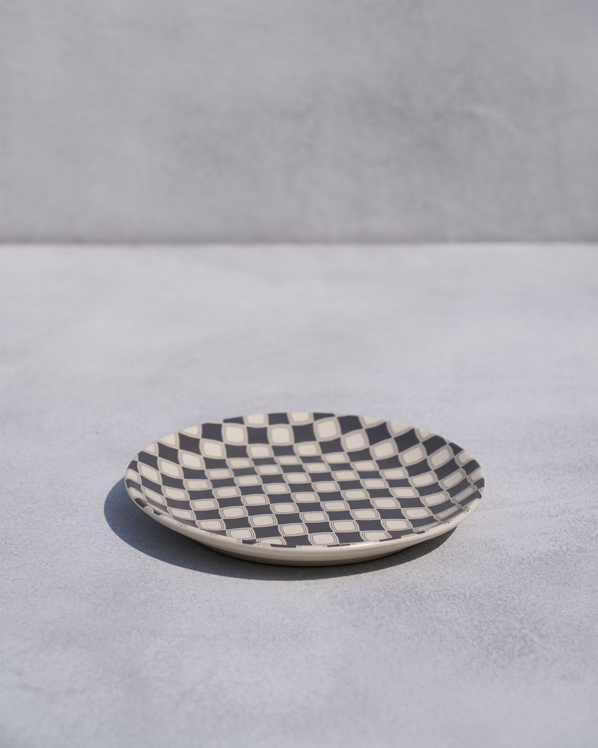 Angled view of a Fez quarter plate with charcoal and cream checker pattern.