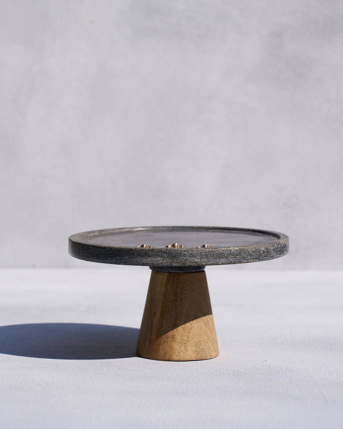Side view of a Firefly cake stand with a dark marble top on a wooden cone base.