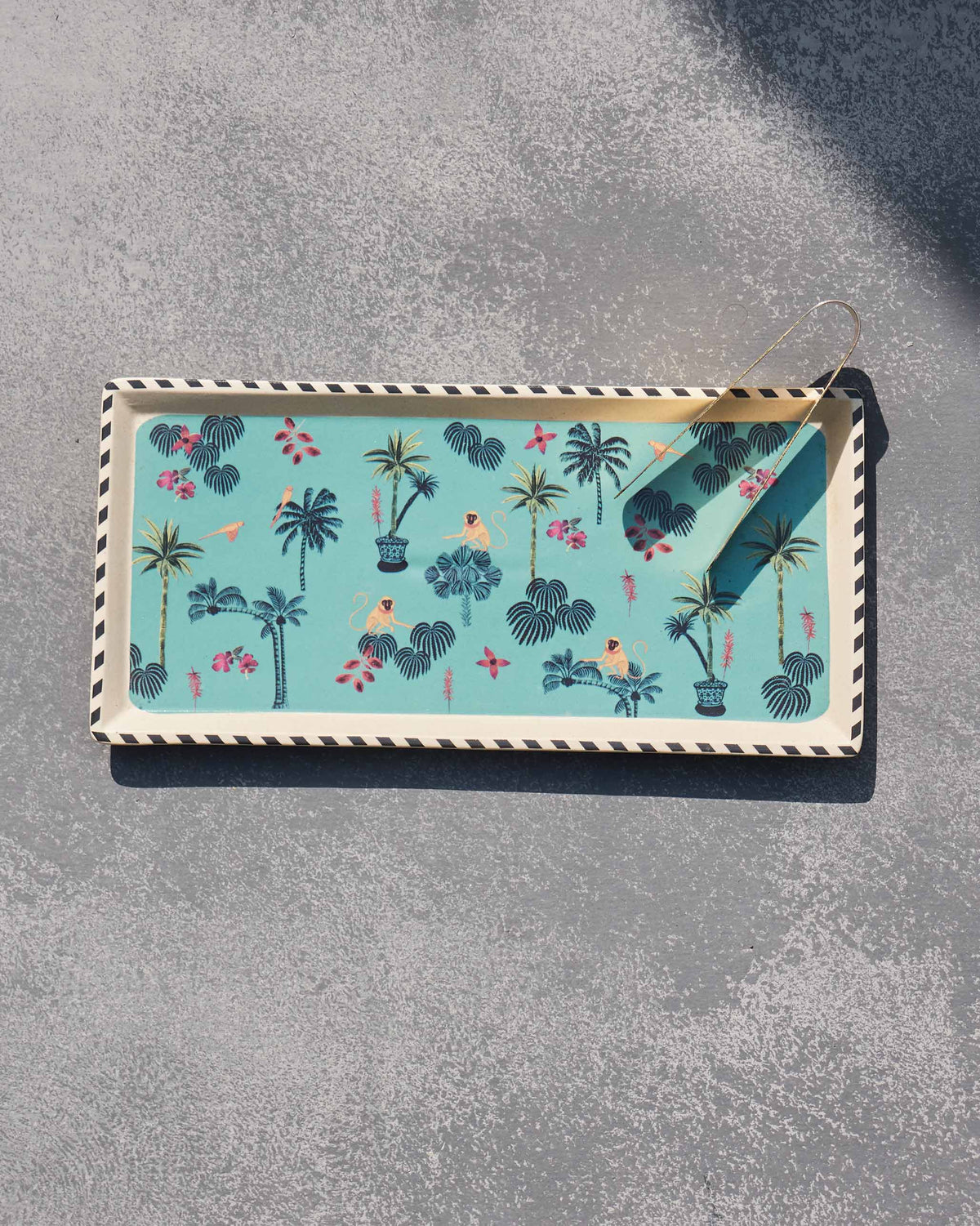 Teal Tropico cookie tray with palm and monkey print and brass tongs.