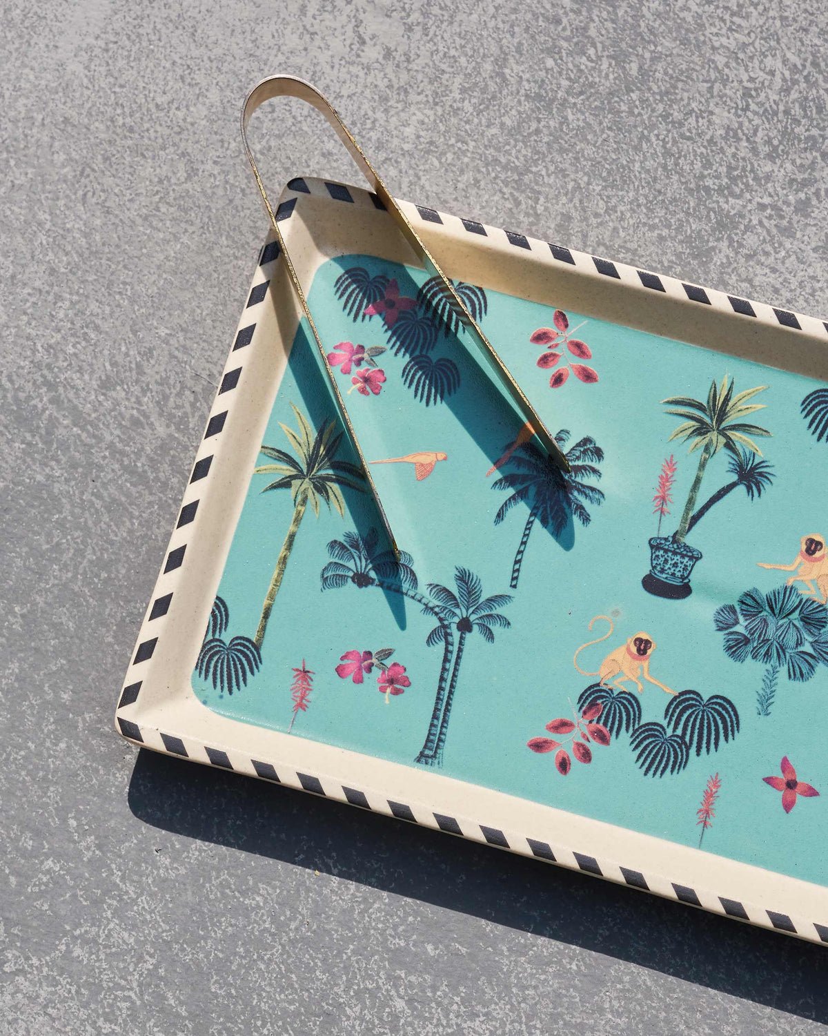 Close-up of monkeys and palms on a teal Tropico cookie tray with tongs.