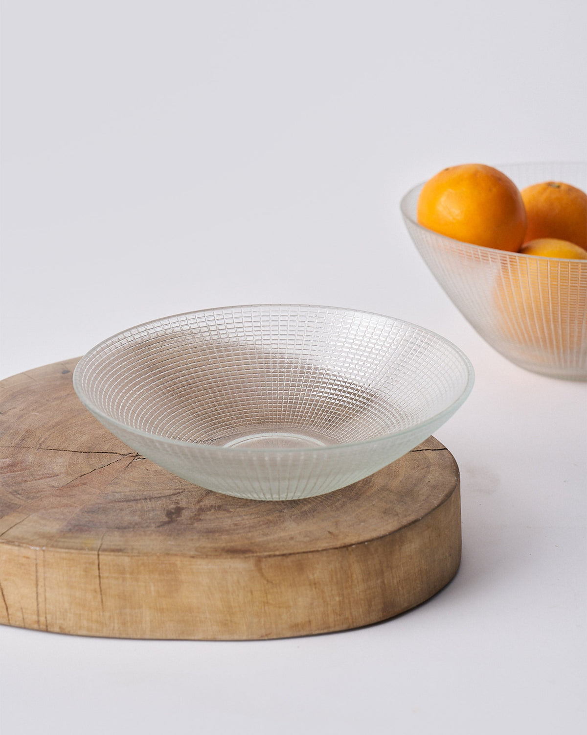 Small clear Aire serving bowl with a grid etch on a round wooden board.