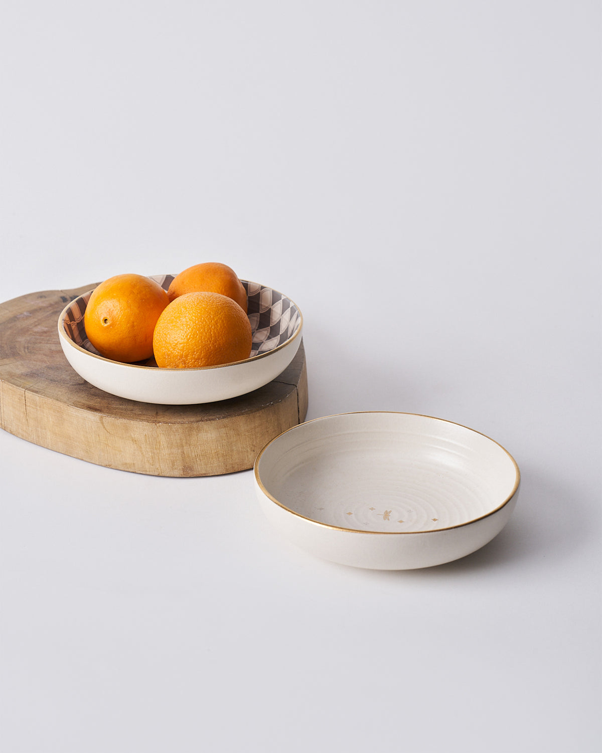 Fez Shallow Bowl with a checkered interior holding oranges beside a cream bowl.