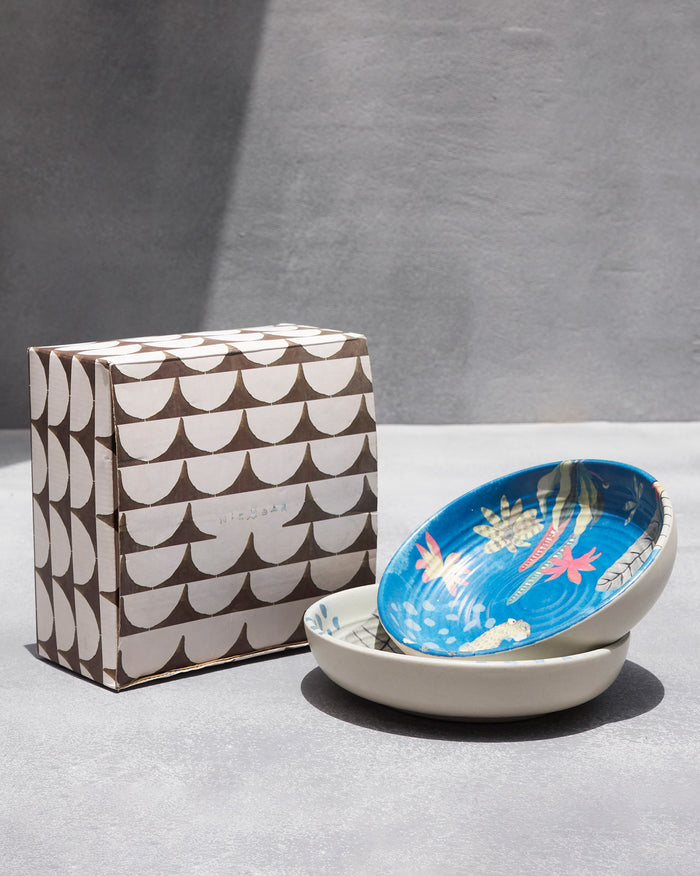 Pair of Mahi shallow bowls with a blue floral interior beside a gift box.