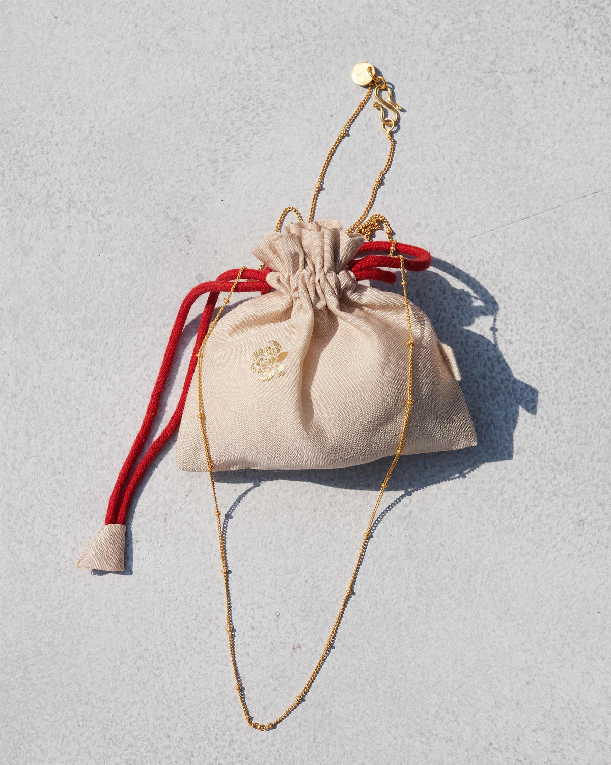 Boondi Chain laid on a beige pouch with a red drawstring.