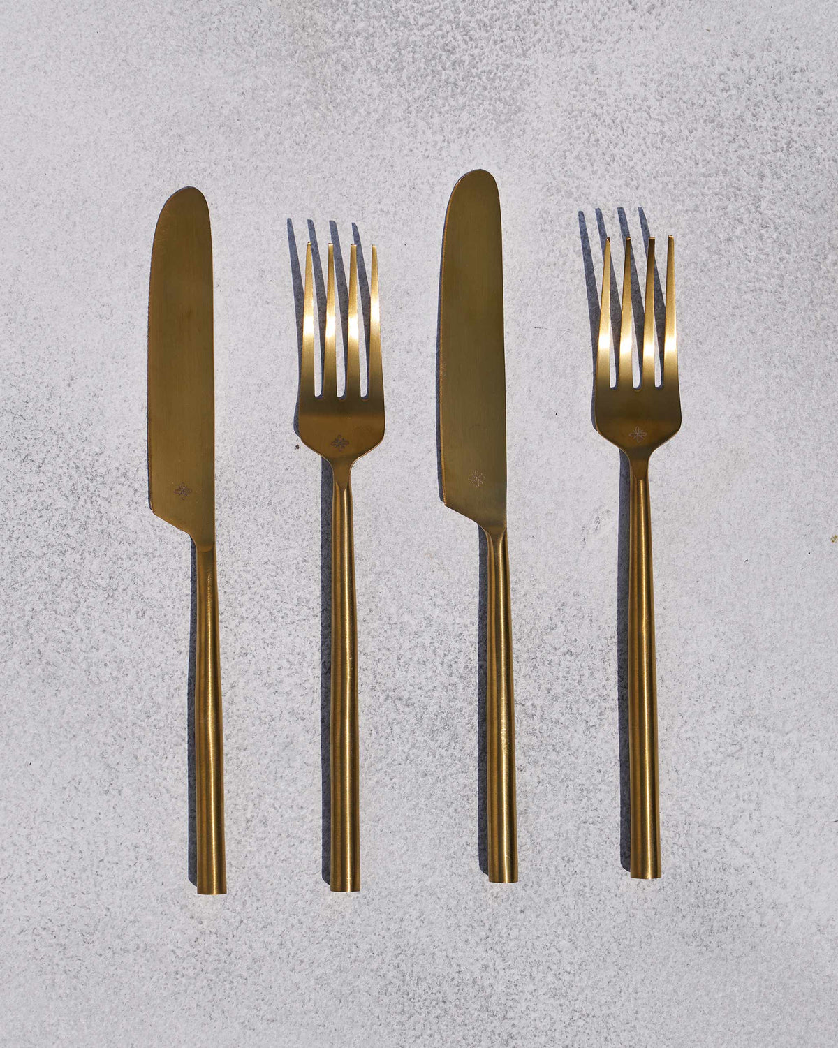 Pair of brushed gold Sitara forks and knives laid flat.