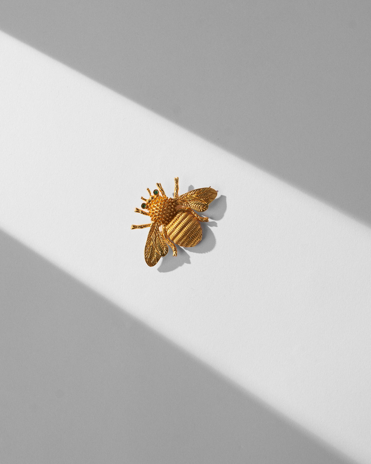 Gold Bee brooch with green stone eyes, textured body and etched wings.