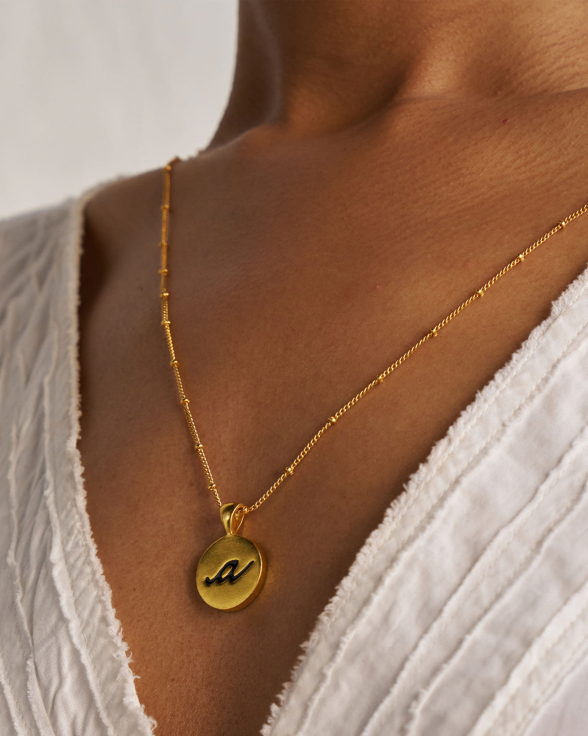 Gold Alphabet A charm with a black script letter a when worn.