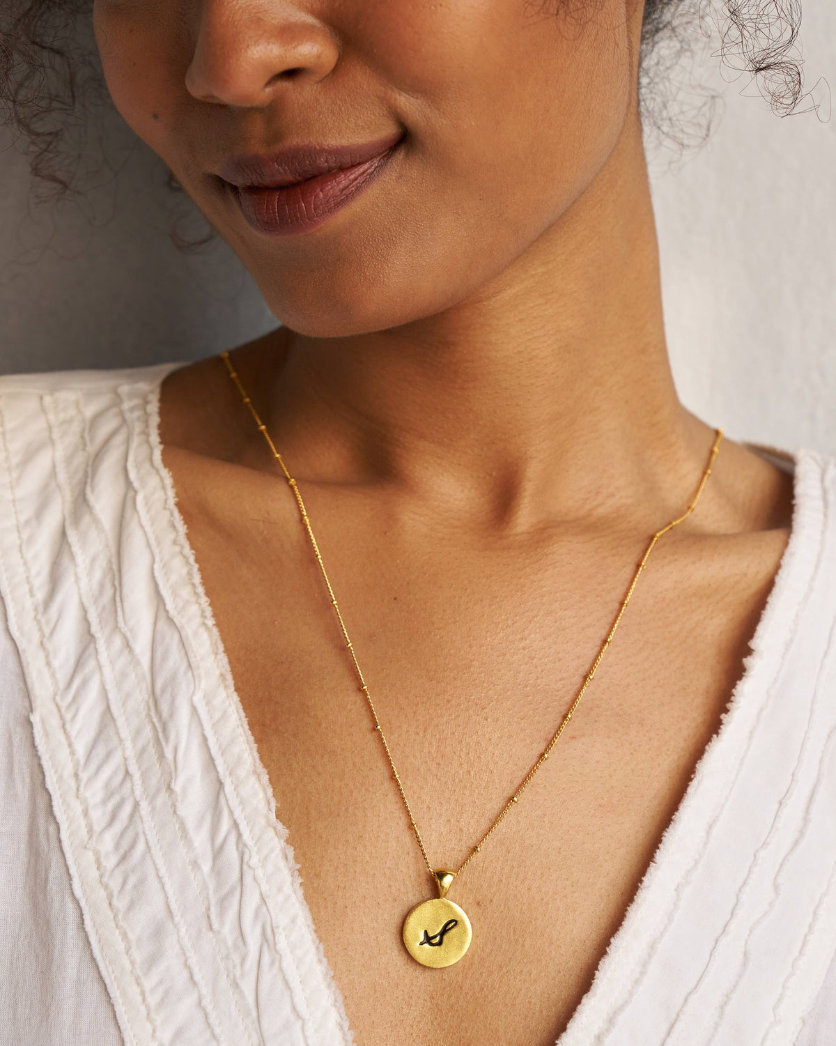 Gold satellite chain with a circular gold charm engraved with a black S.